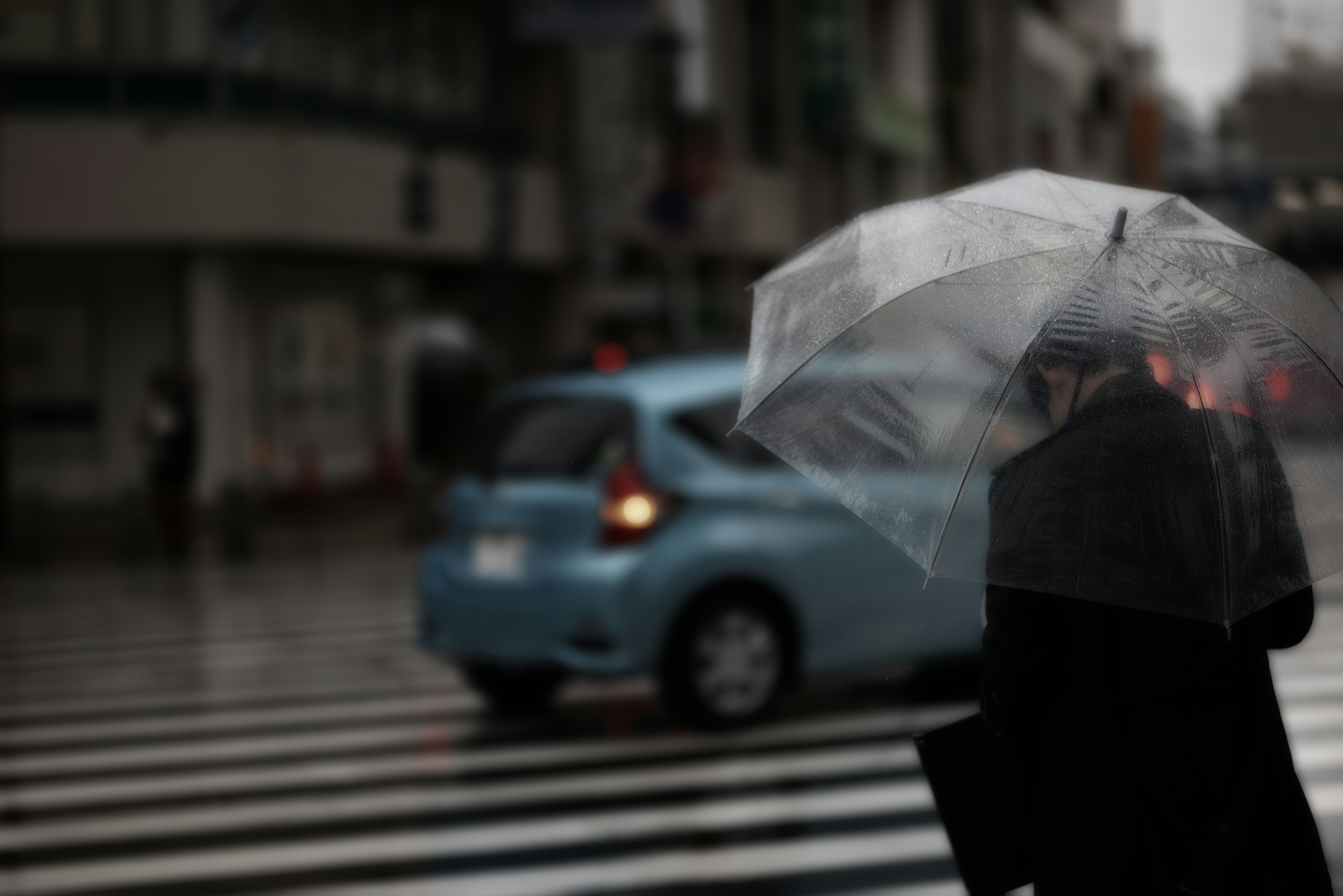 Une personne traversant la rue avec un parapluie transparent sous la pluie