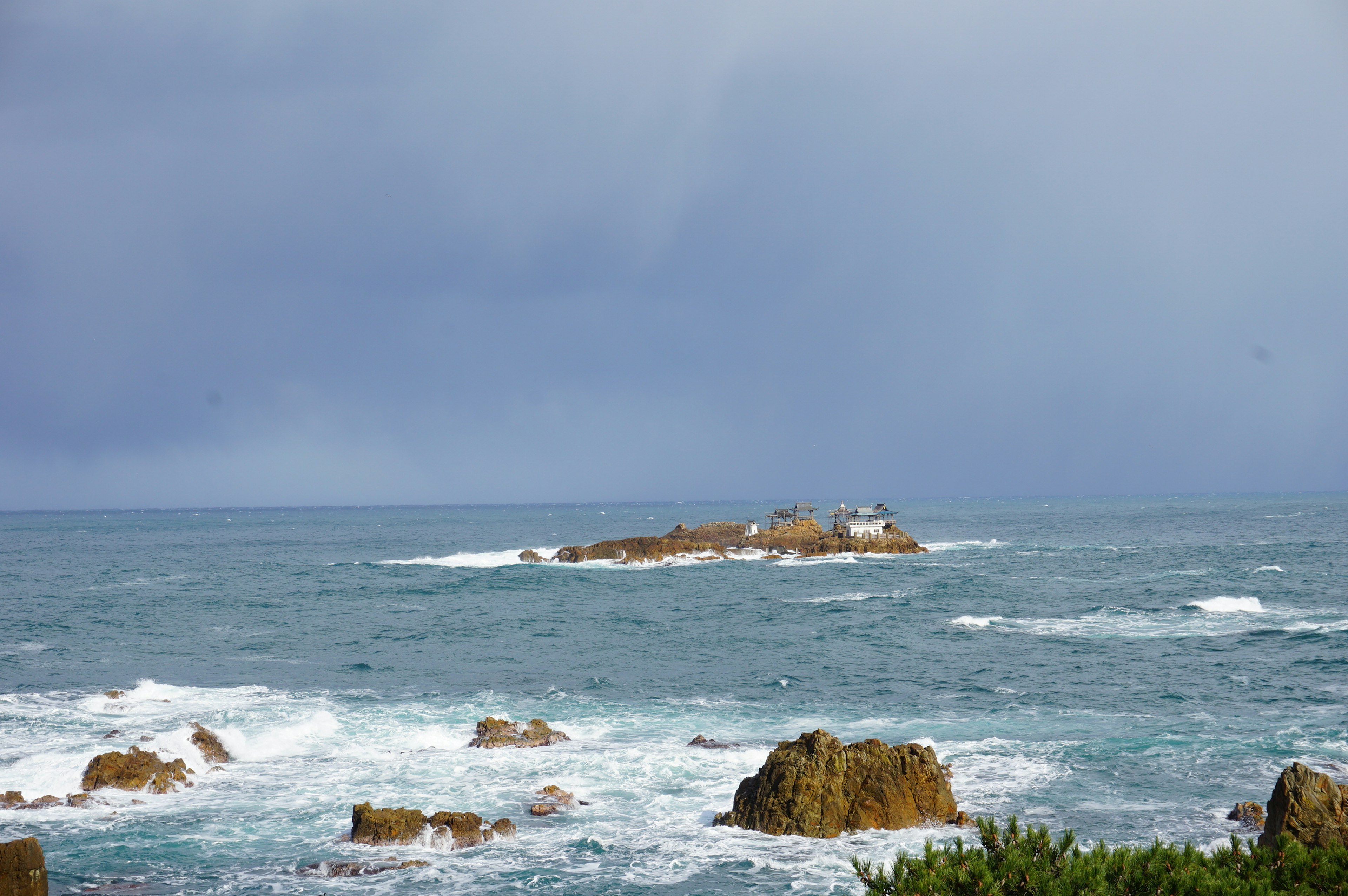 Vista del océano azul con costa rocosa e una pequeña isla