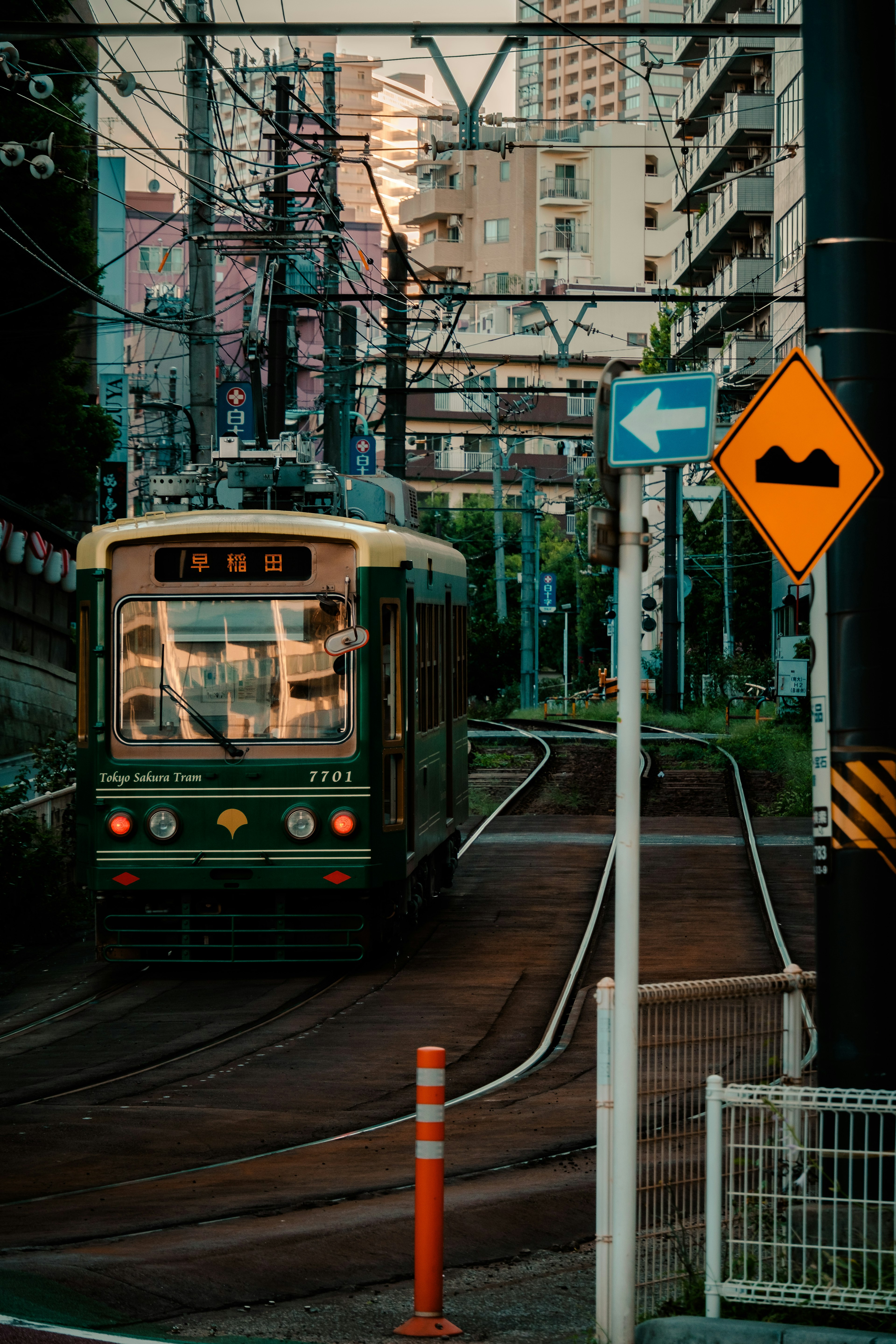 Green streetcar navigating through a cityscape with sunset reflections buildings and power lines visible