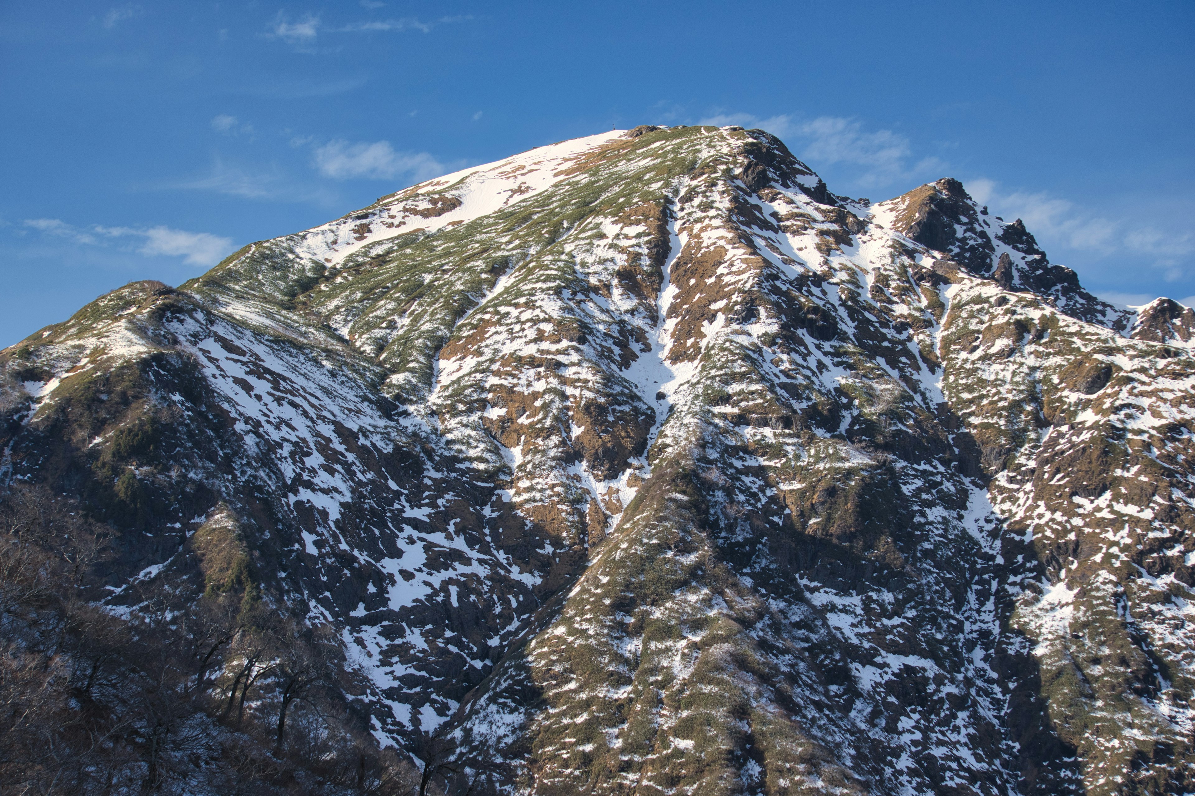 Paisaje montañoso cubierto de nieve con cielo azul claro y nubes dispersas