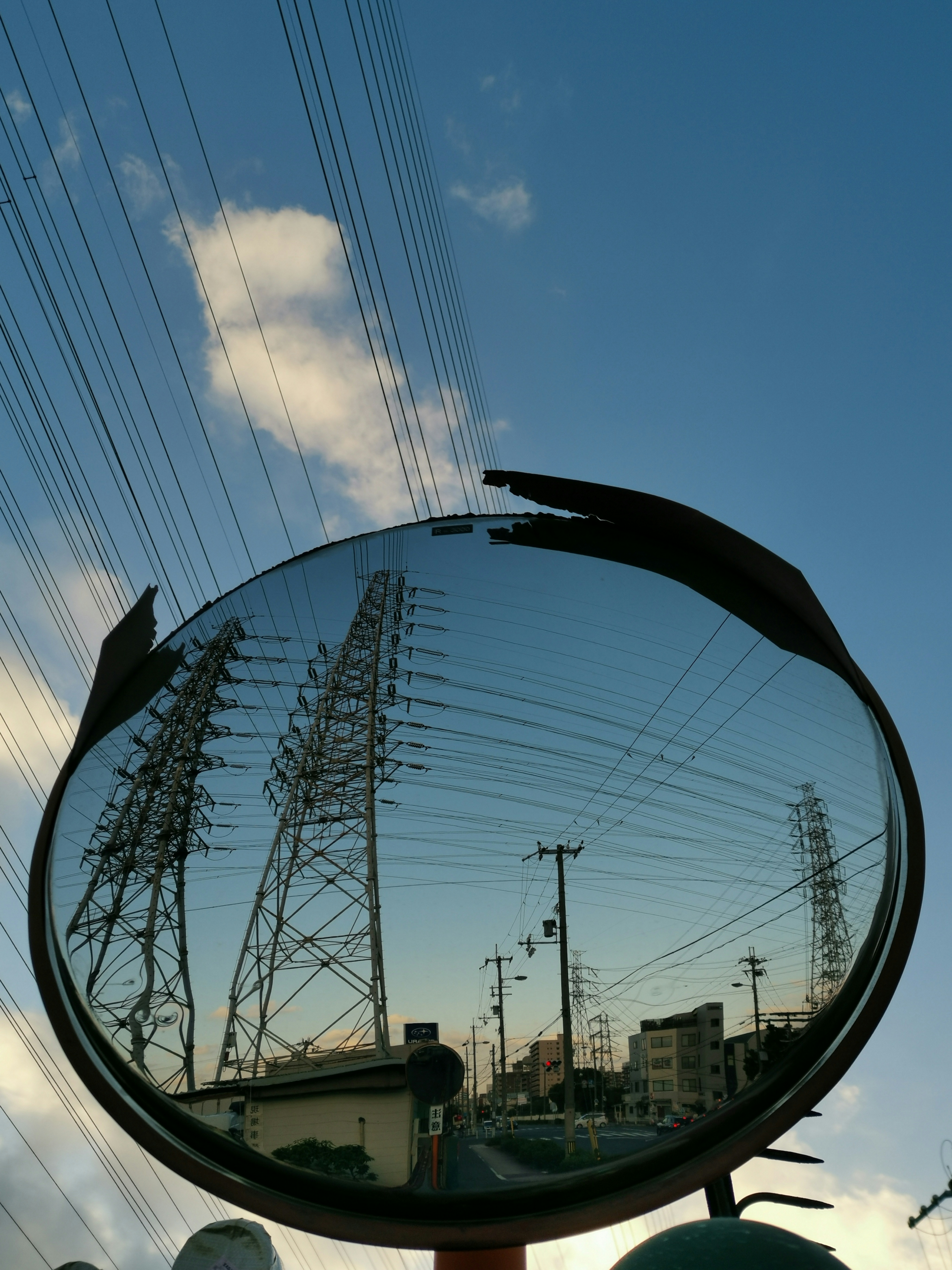 Reflection of power poles and sky in a roadside mirror