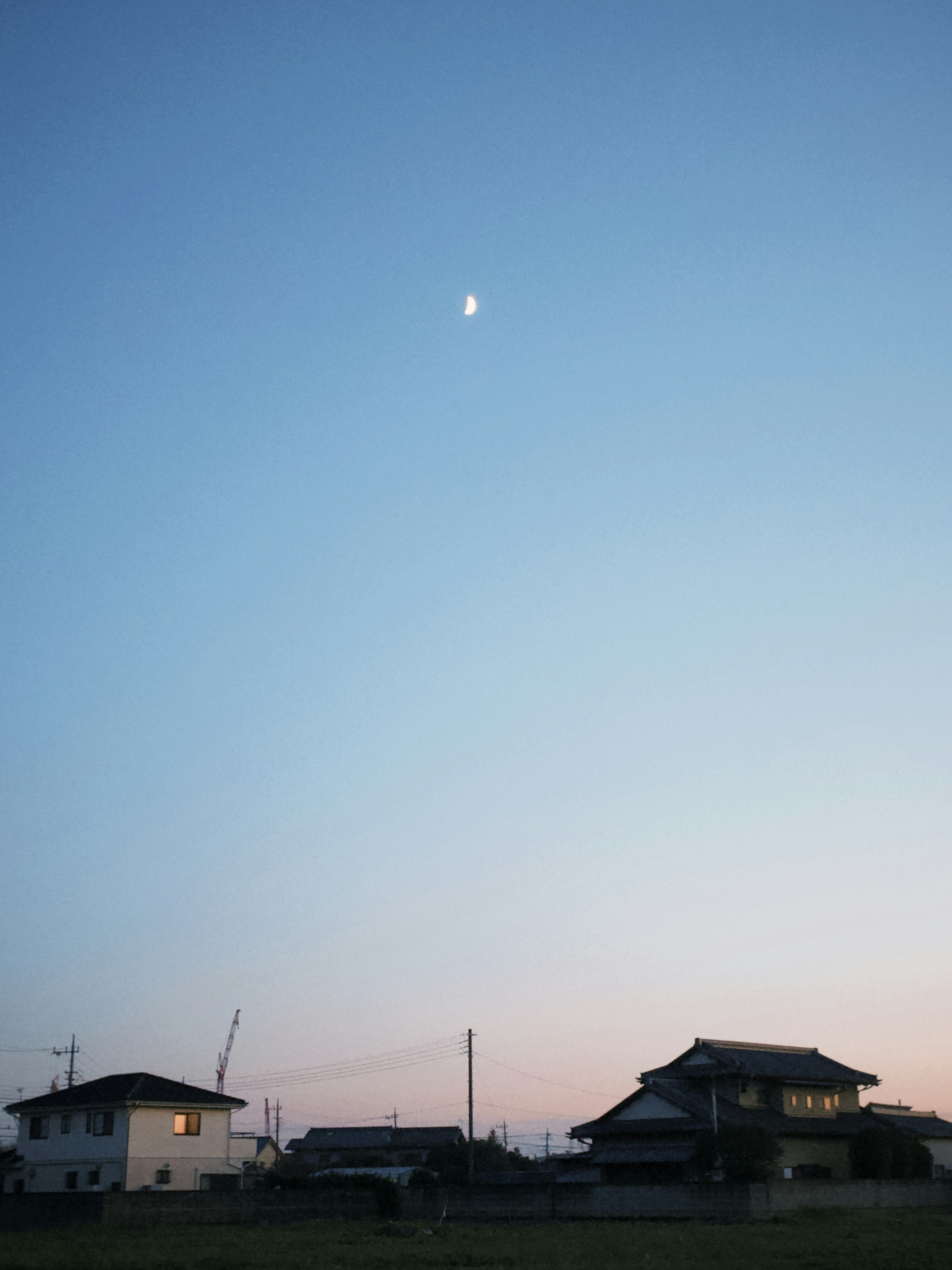 夕暮れの空に浮かぶ月と住宅