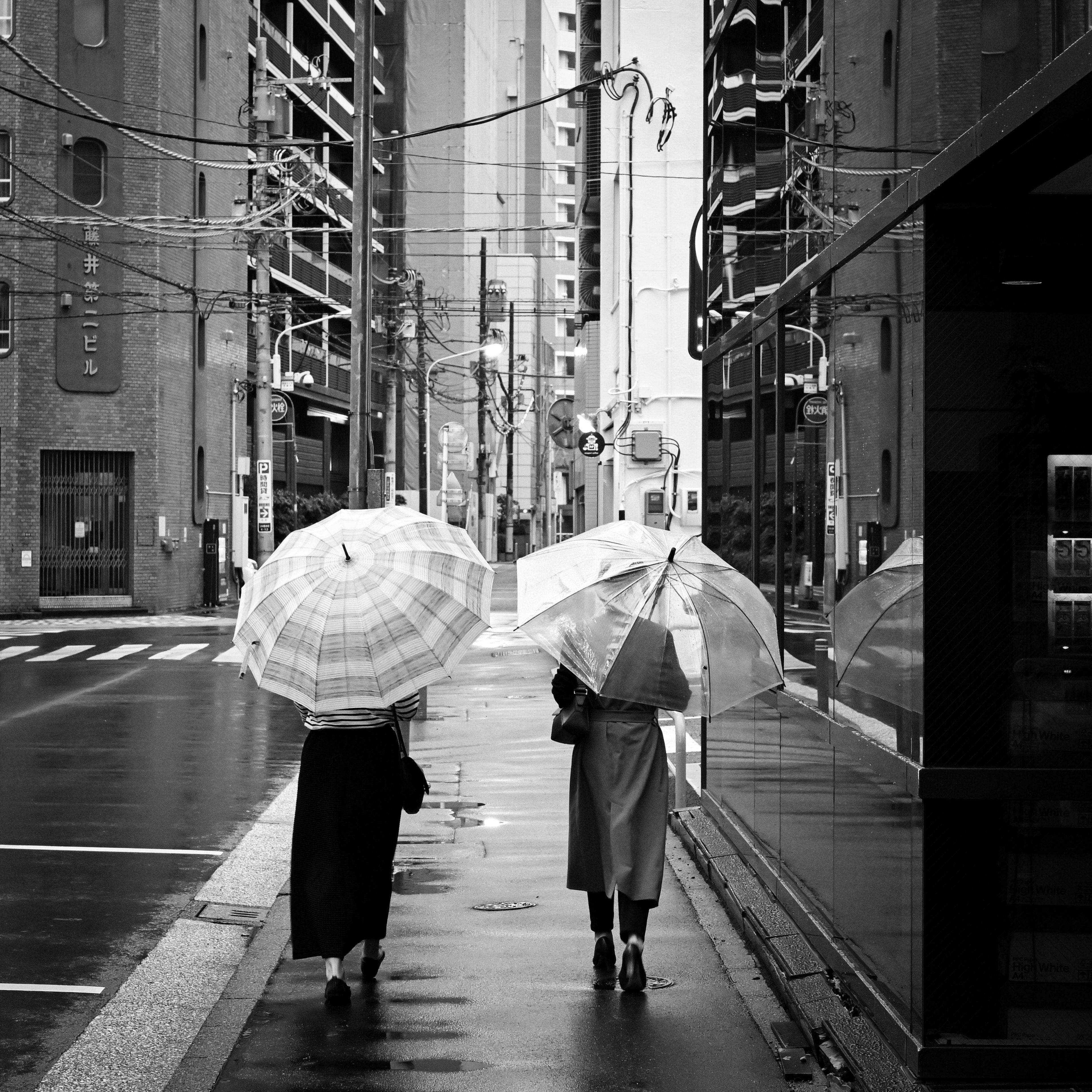 Two women walking in the city holding umbrellas in a black and white scene