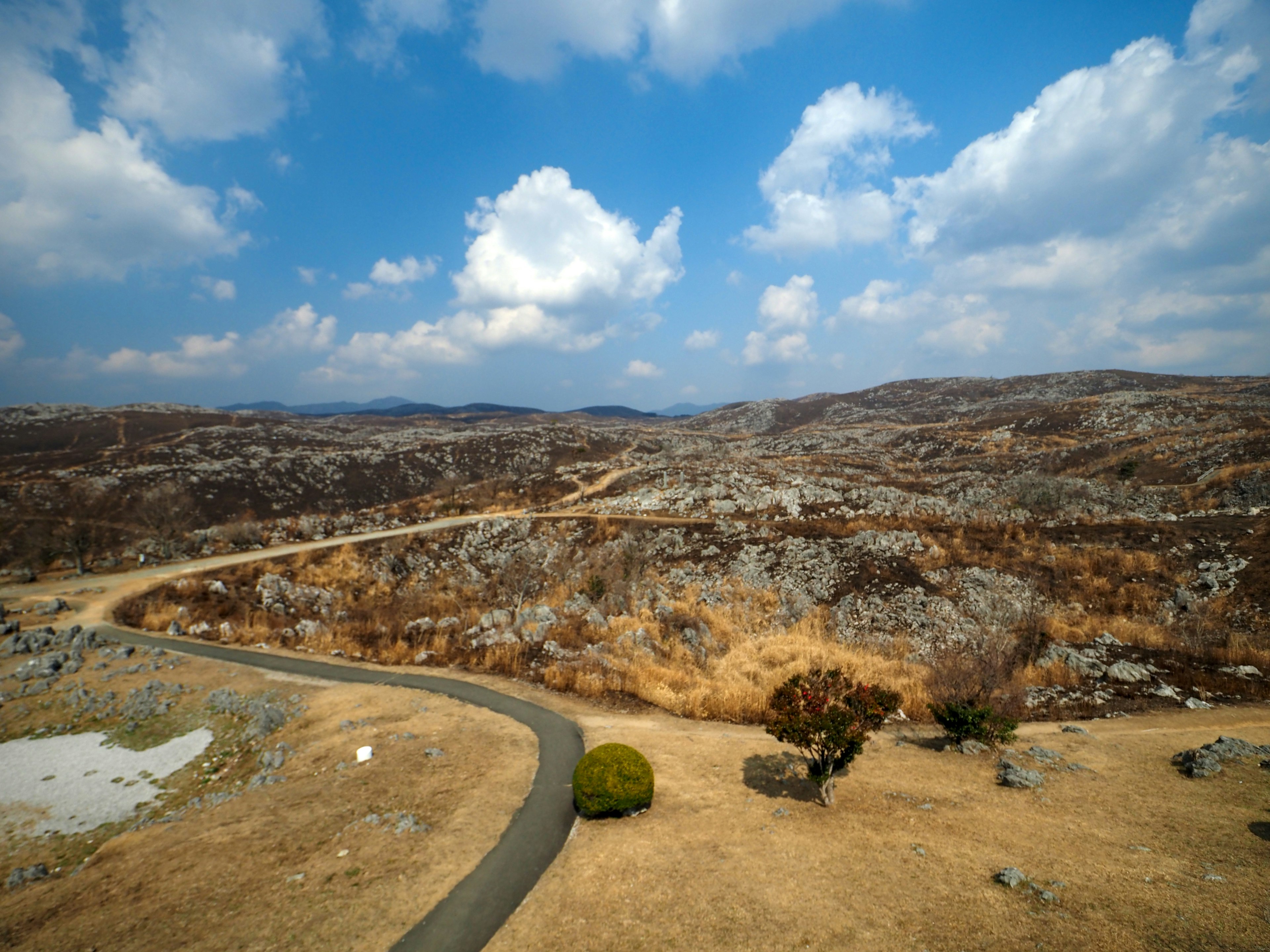 Paisaje seco con colinas onduladas y cielo azul, con hierba dispersa y rocas