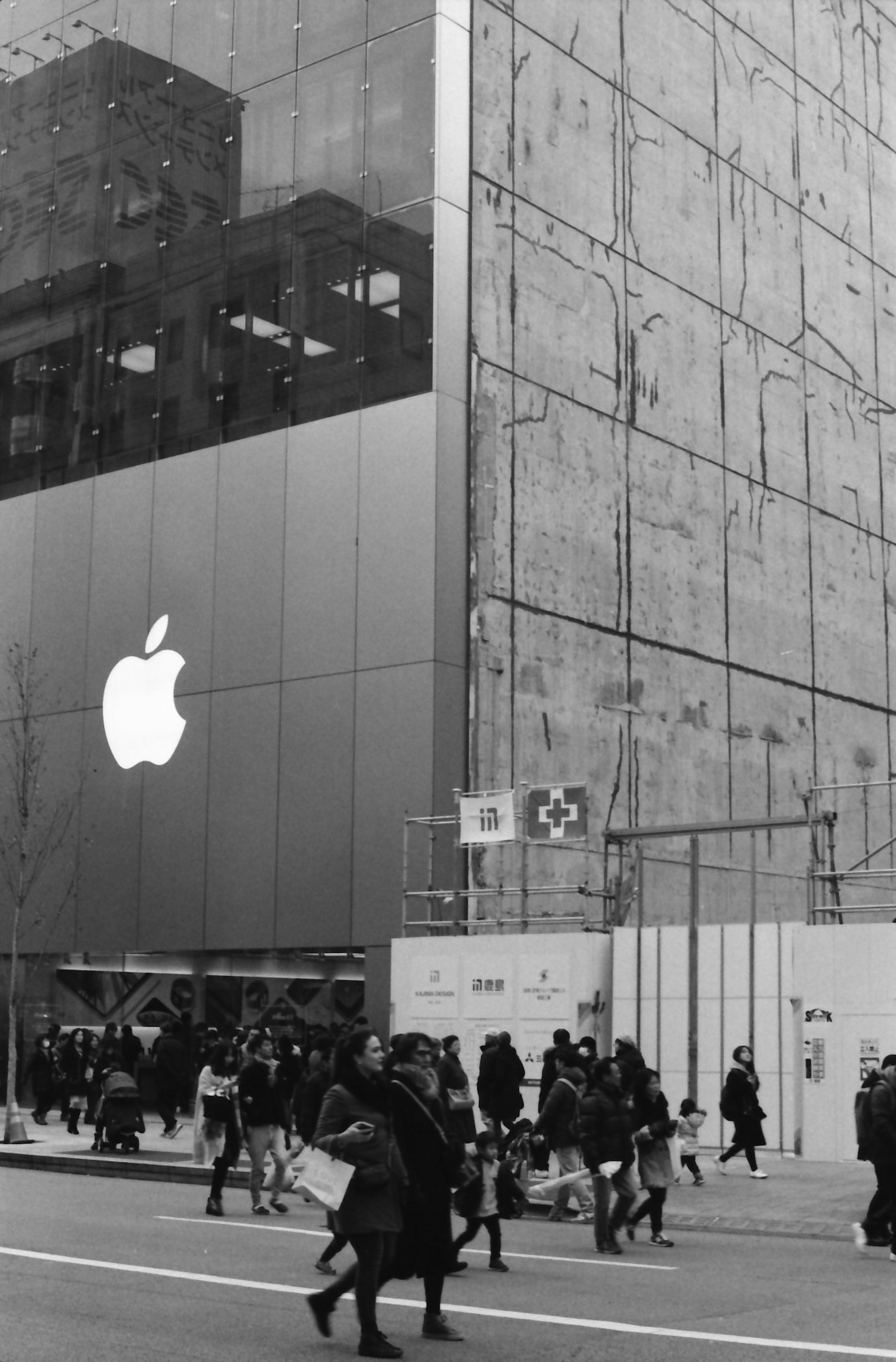 Black and white scene of people walking past a building with a prominent Apple logo