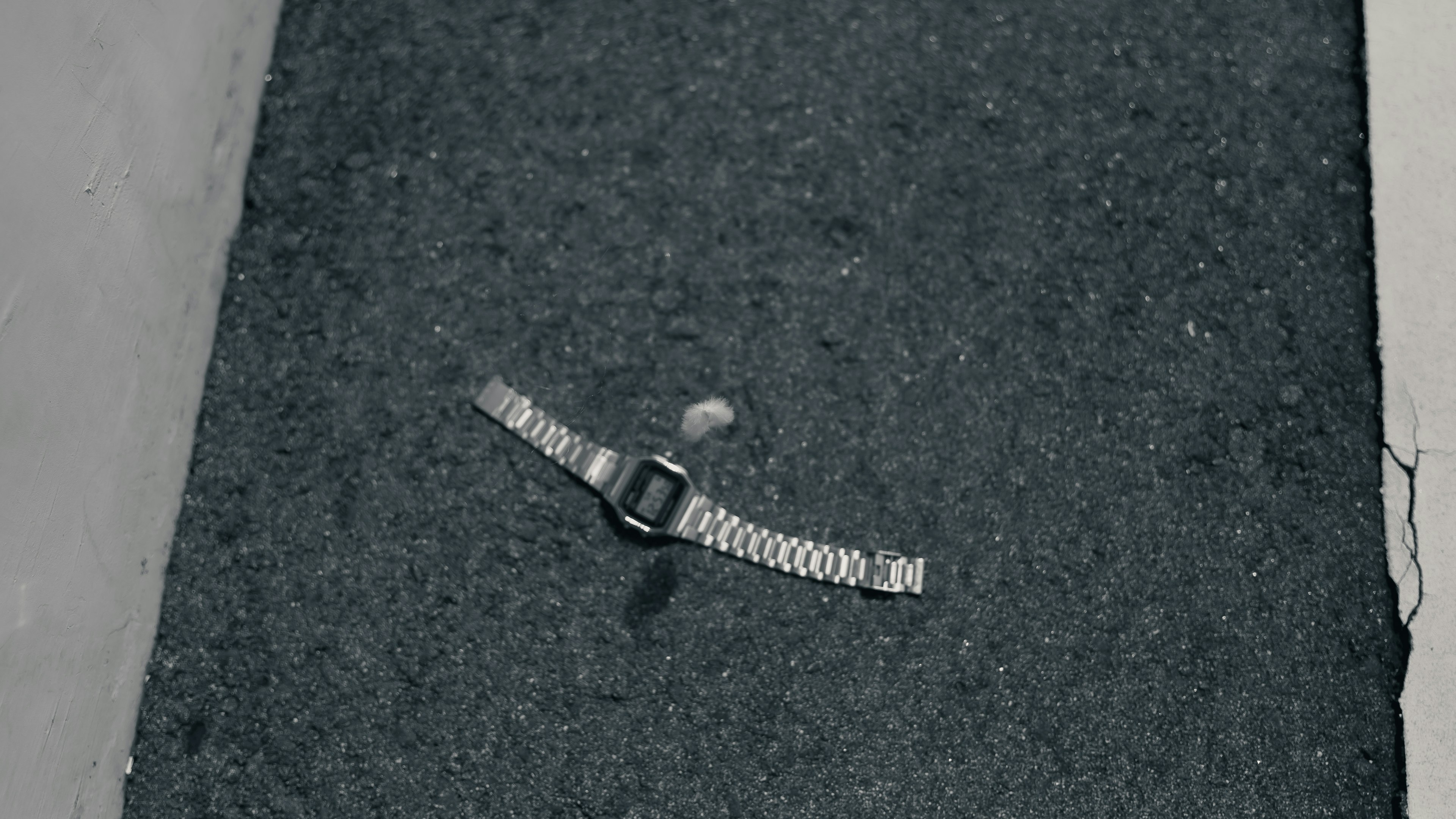 A watch with a metallic band placed on black asphalt