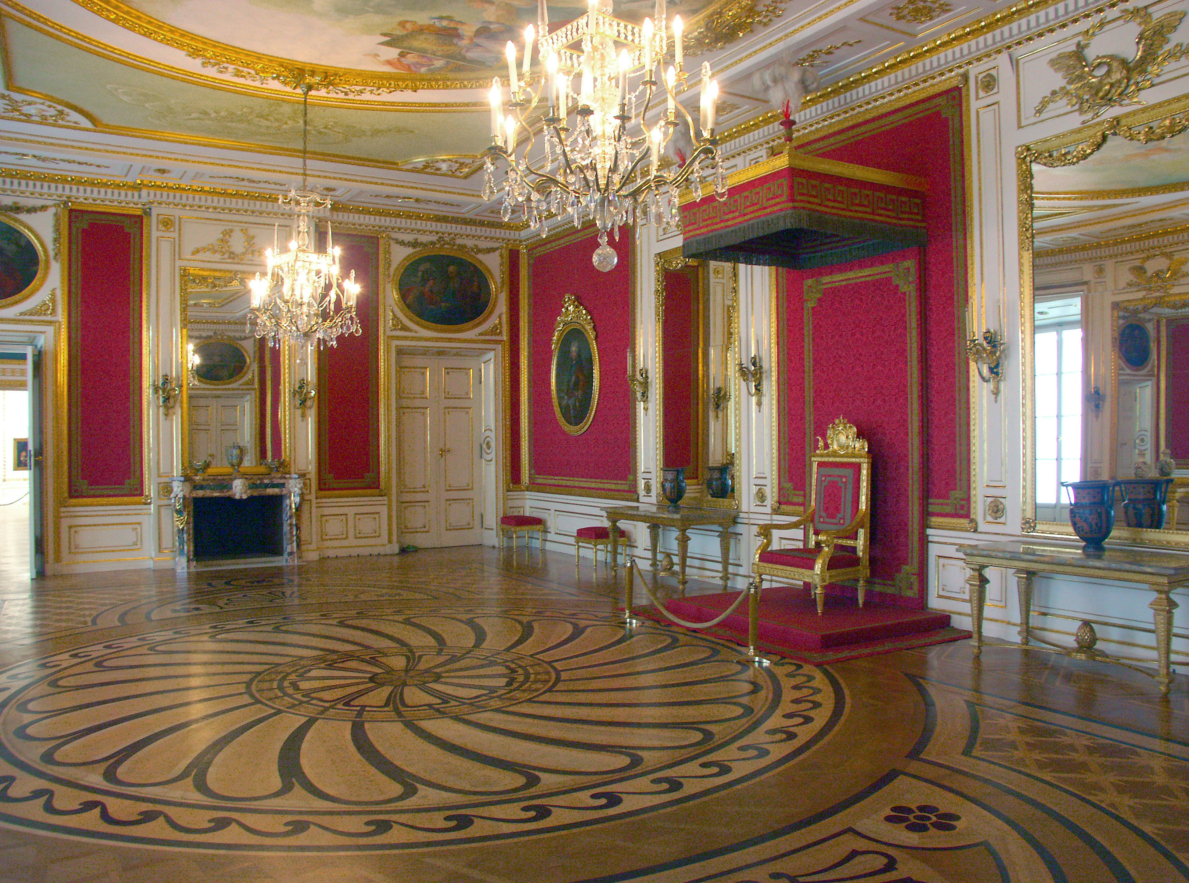 Habitación espaciosa con candelabros lujosos y paredes rojas Piso con un hermoso patrón