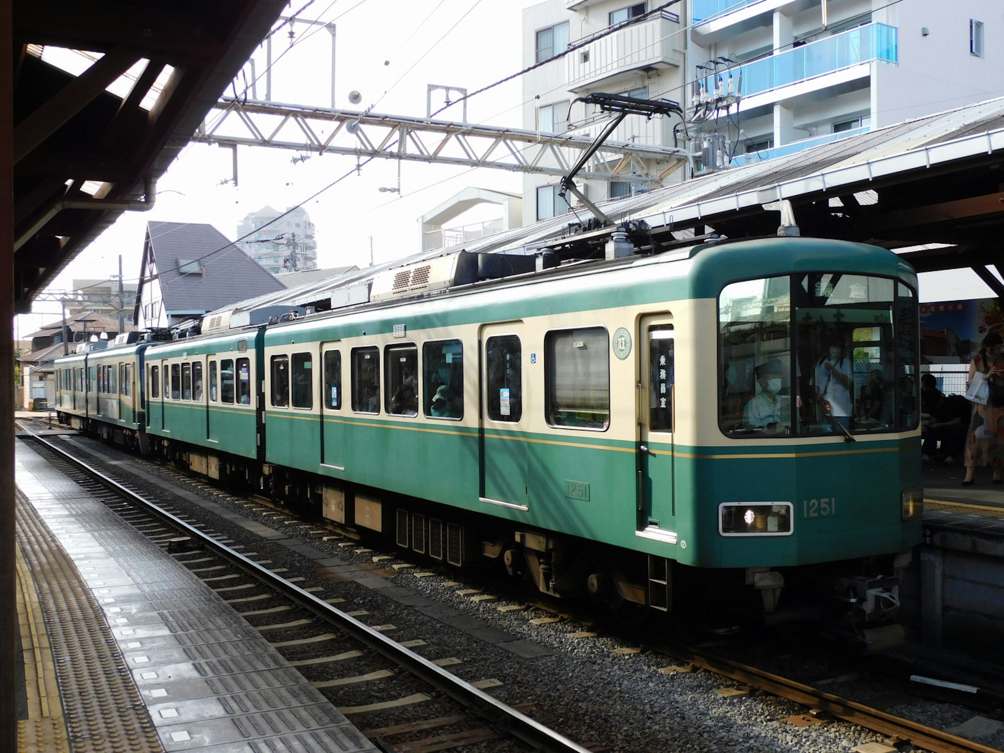 綠色火車停靠在車站，背景有建築物