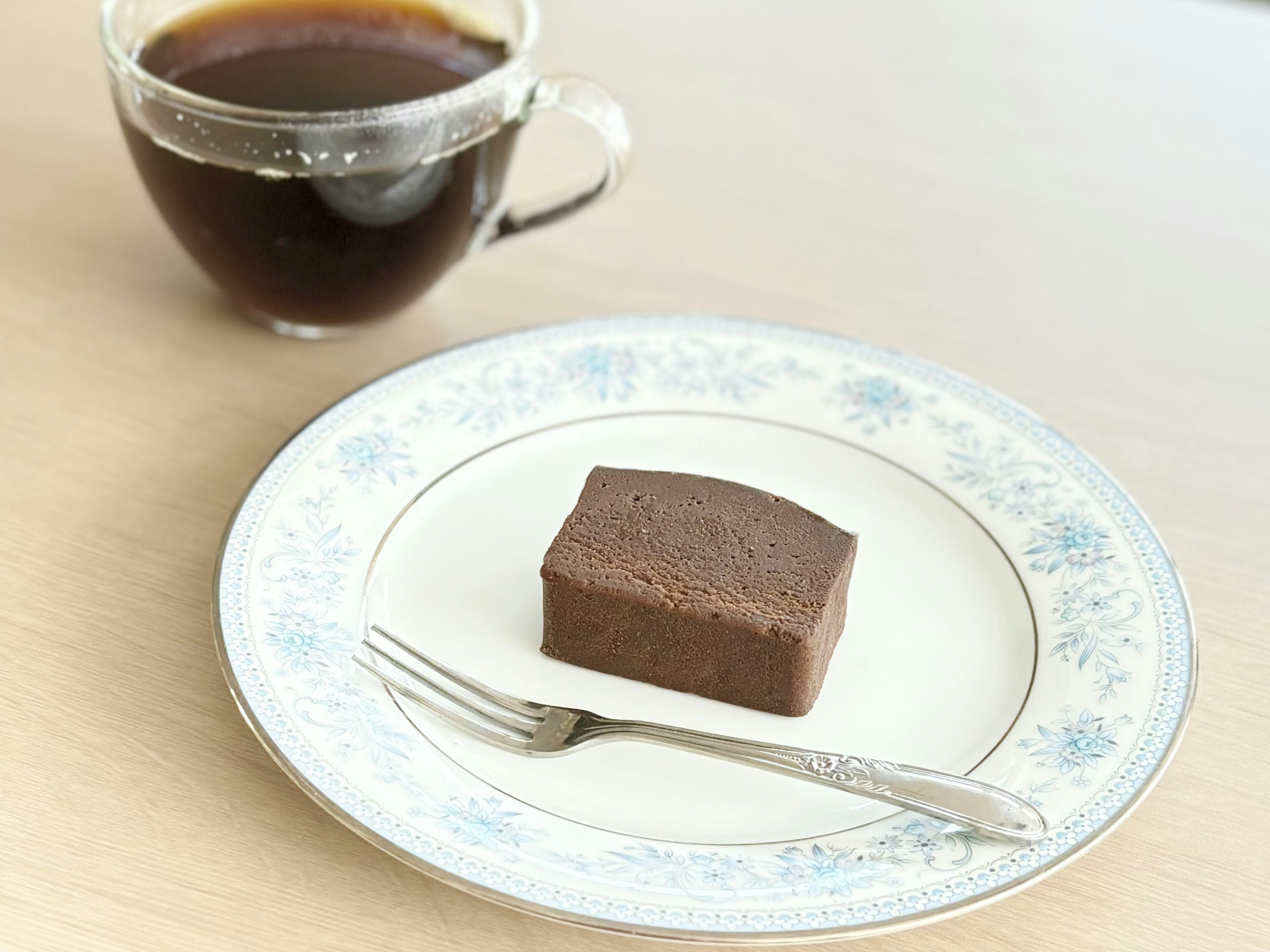 A cup of coffee next to a chocolate cake on a decorative plate