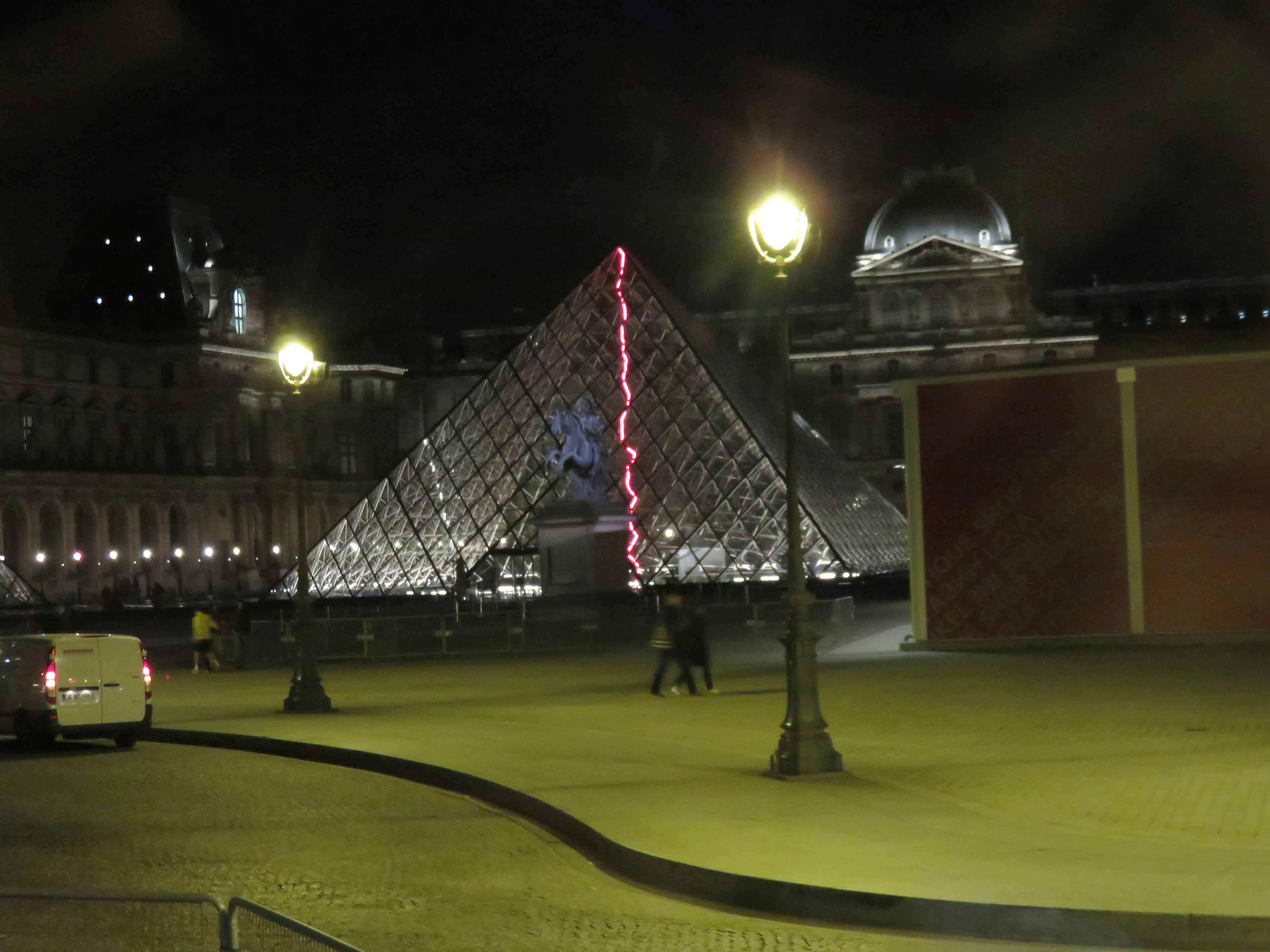 Pemandangan malam Museum Louvre dengan piramida kaca dan lampu jalan