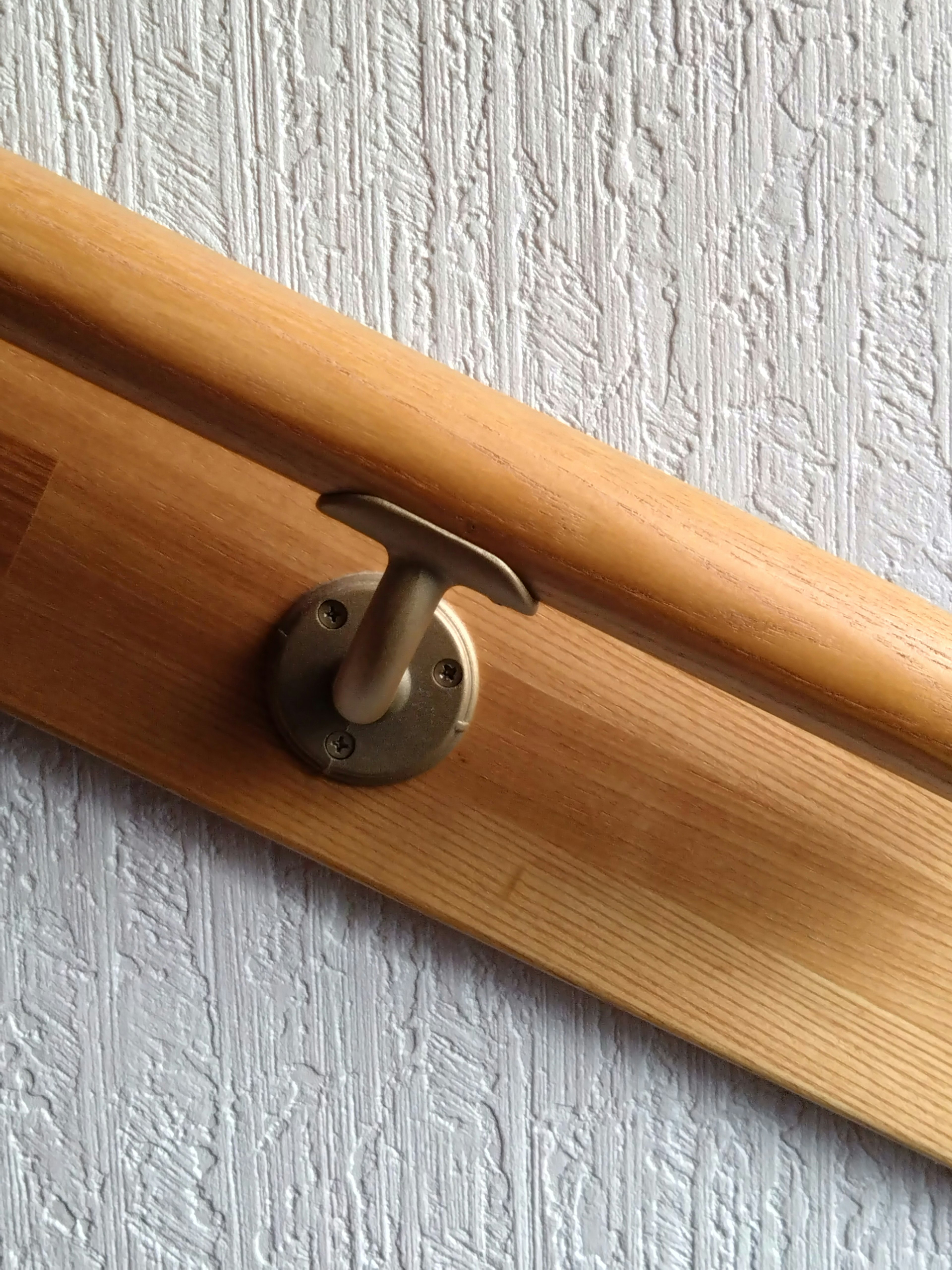 Un gancho de madera montado en una pared texturizada con un mango de metal