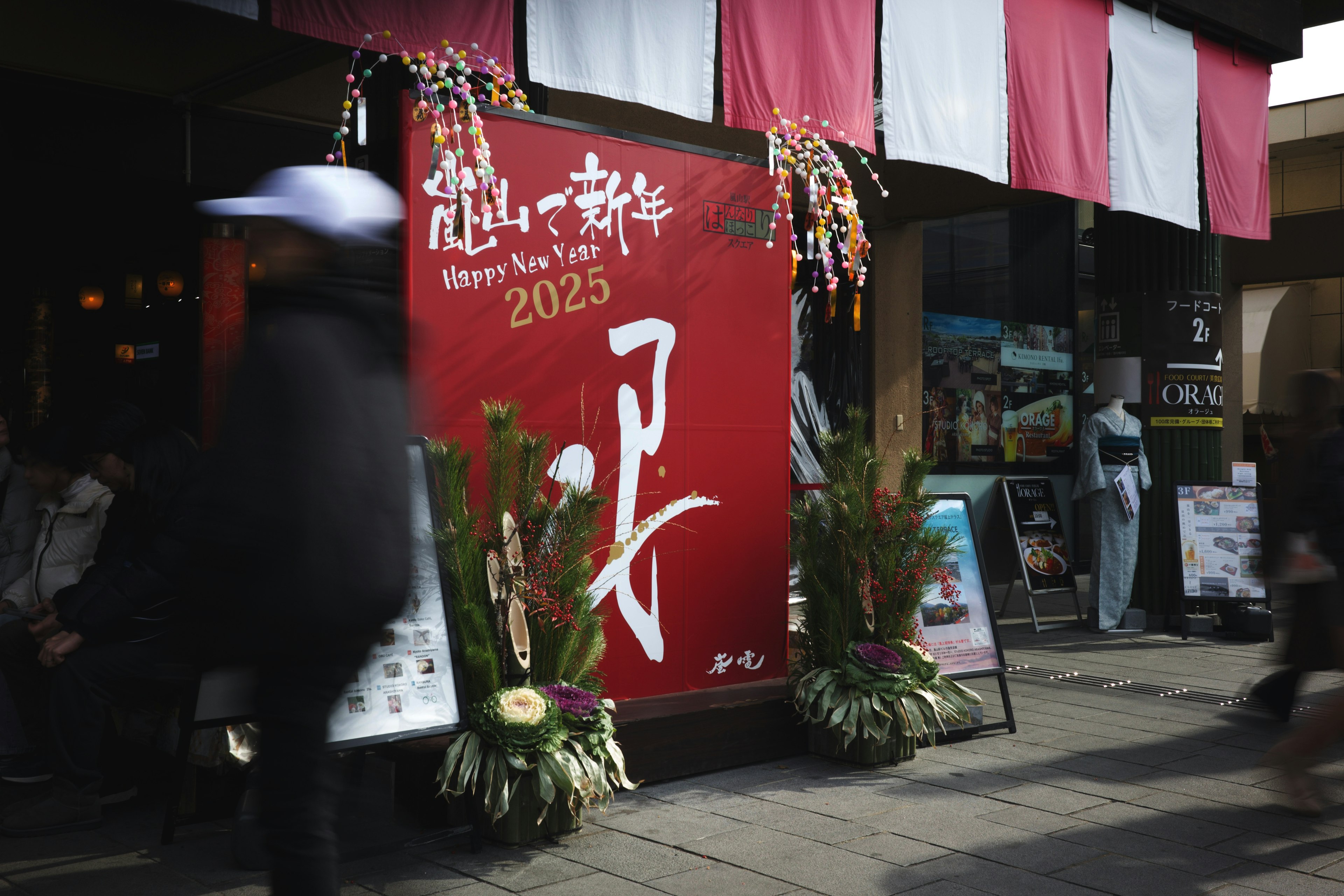 Un panneau rouge décoré pour le Nouvel An affiche l'année 2025 entouré de personnes qui passent