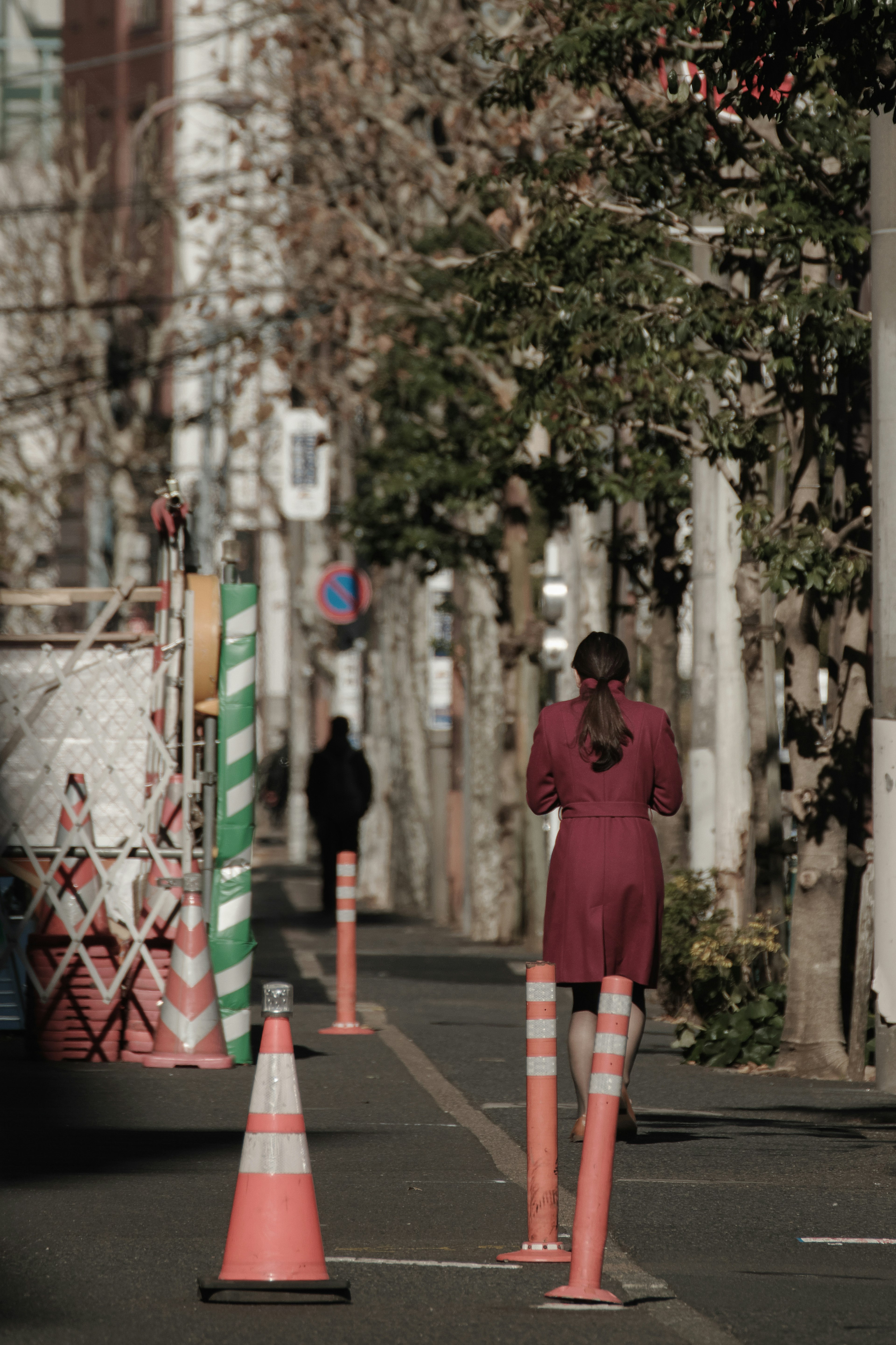 Una donna in abito rosso che cammina lungo una strada fiancheggiata da alberi e segnali di costruzione