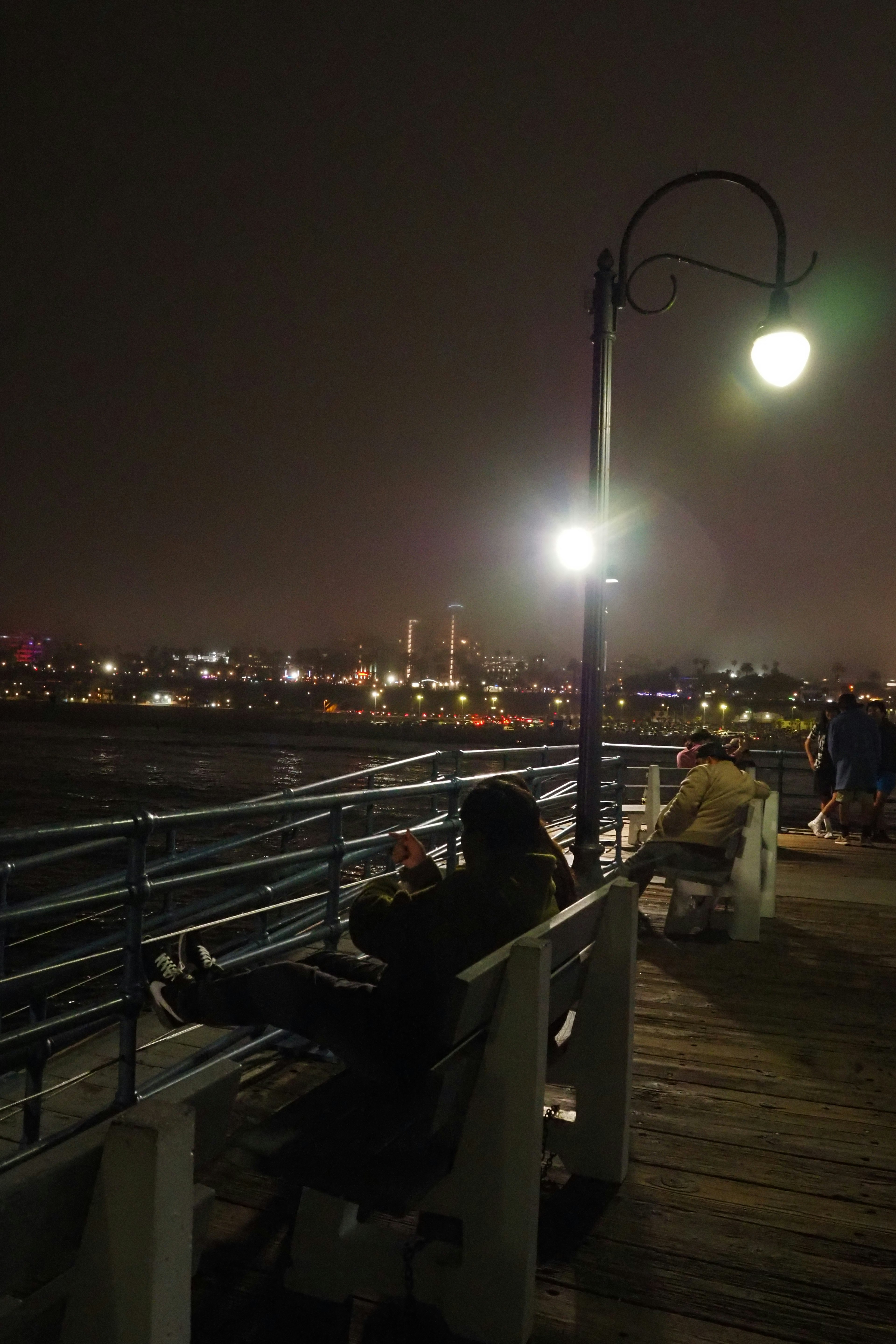 Menschen sitzen nachts auf einem Pier mit Stadtlichtern im Hintergrund