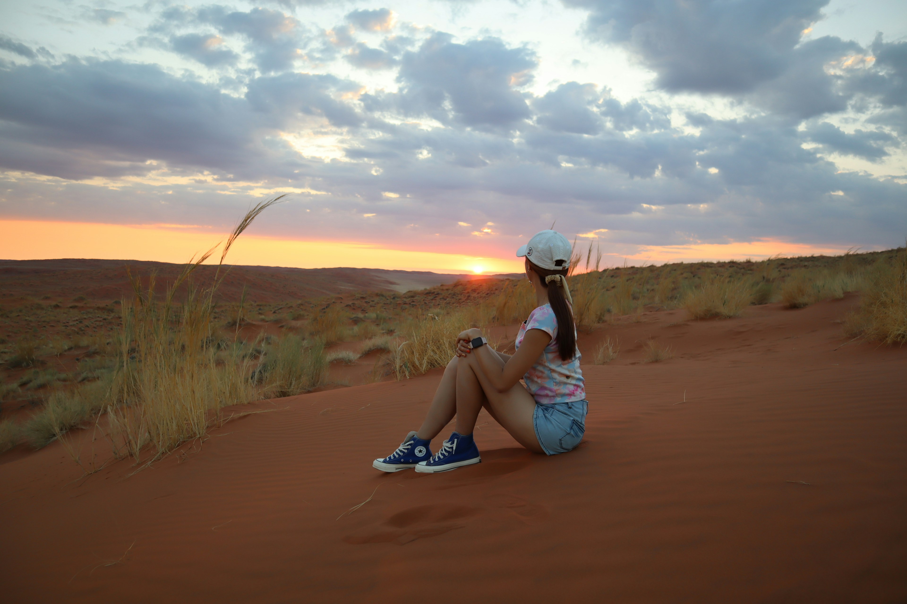 Eine Frau sitzt auf einer Sanddüne und schaut den Sonnenuntergang an