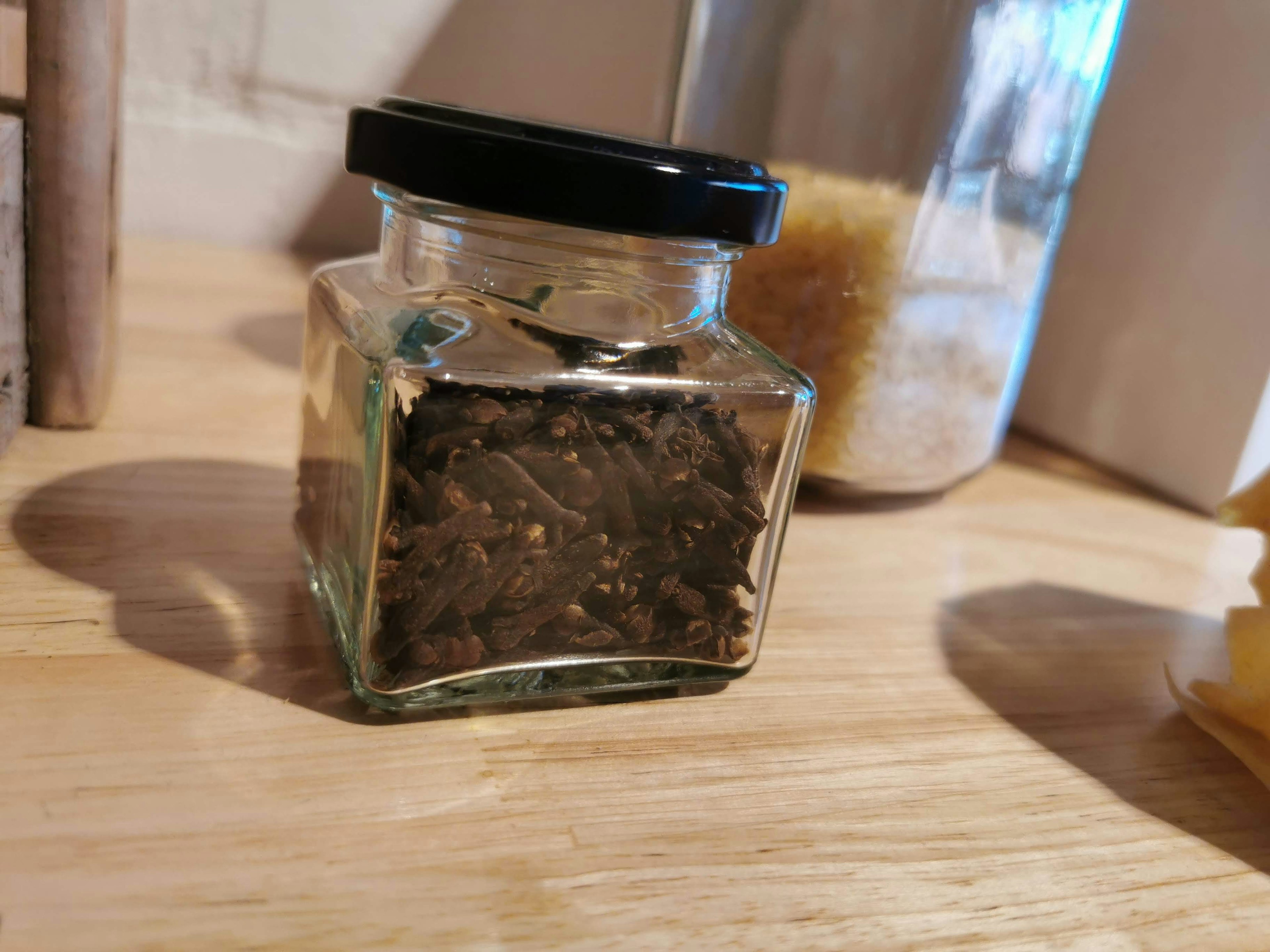 A small glass jar containing dried herbs with a black lid