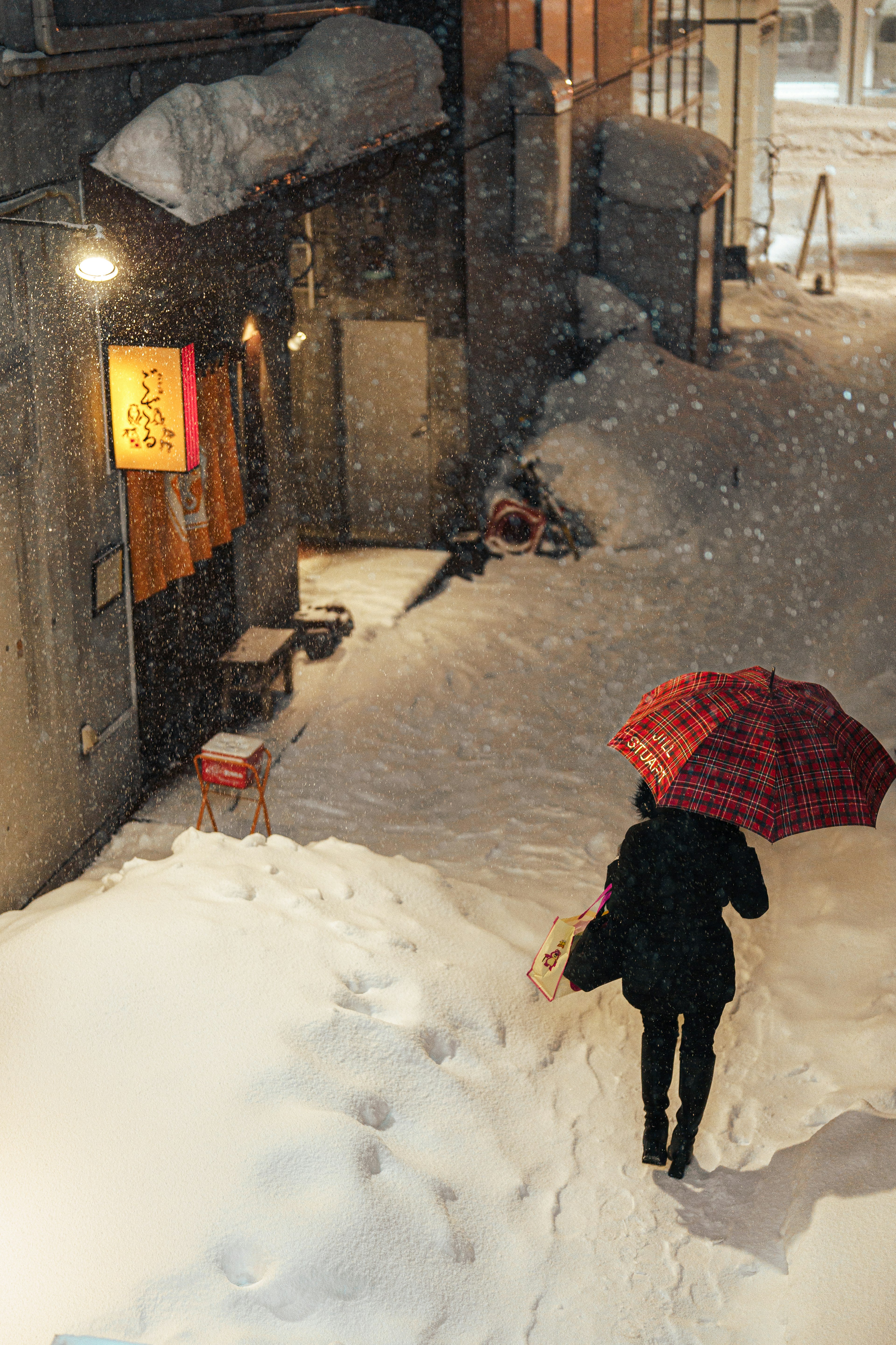 雪の中を歩く人と赤いチェックの傘の風景