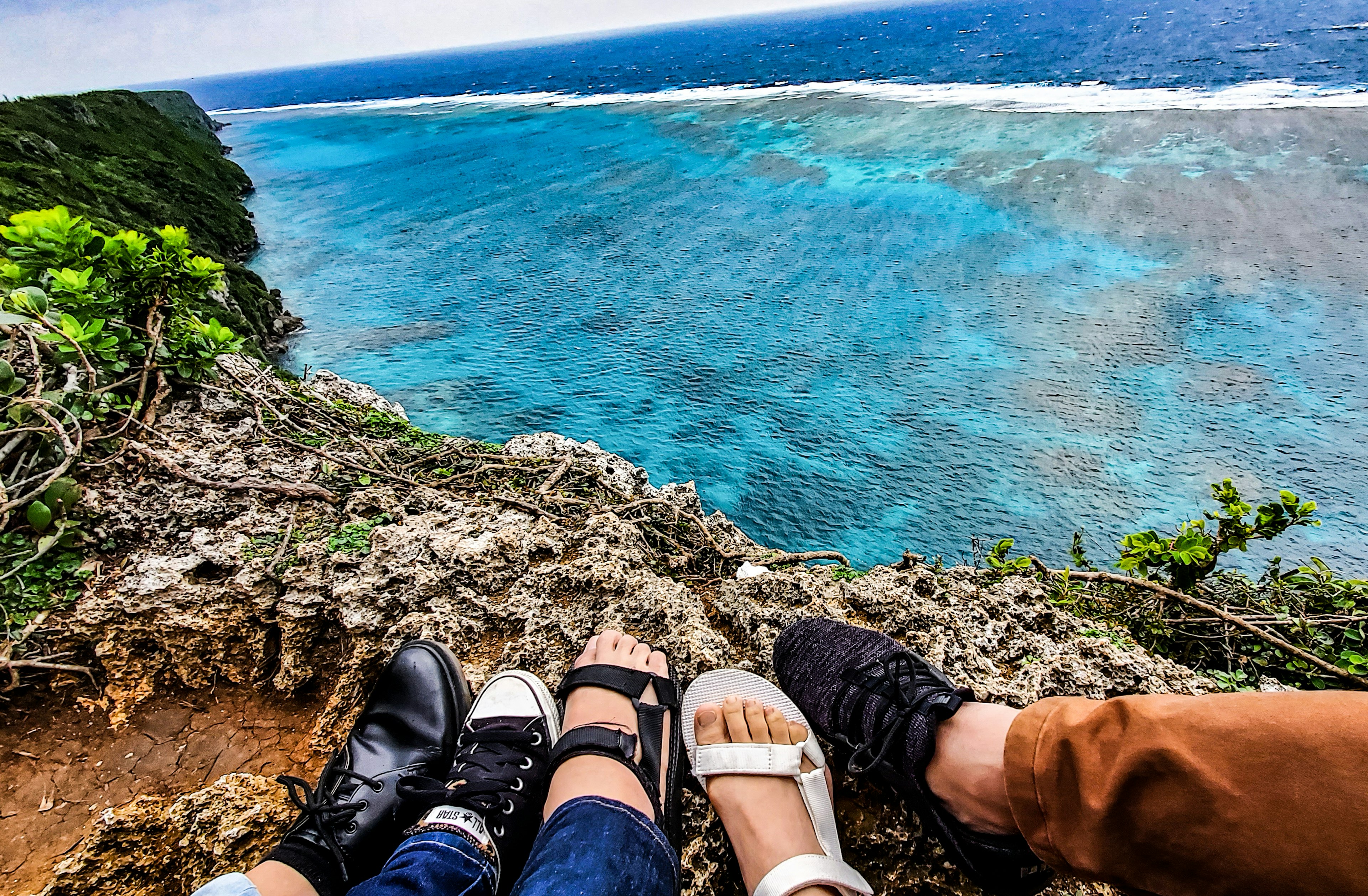 Feet of four people overlooking a blue ocean from a rocky cliff