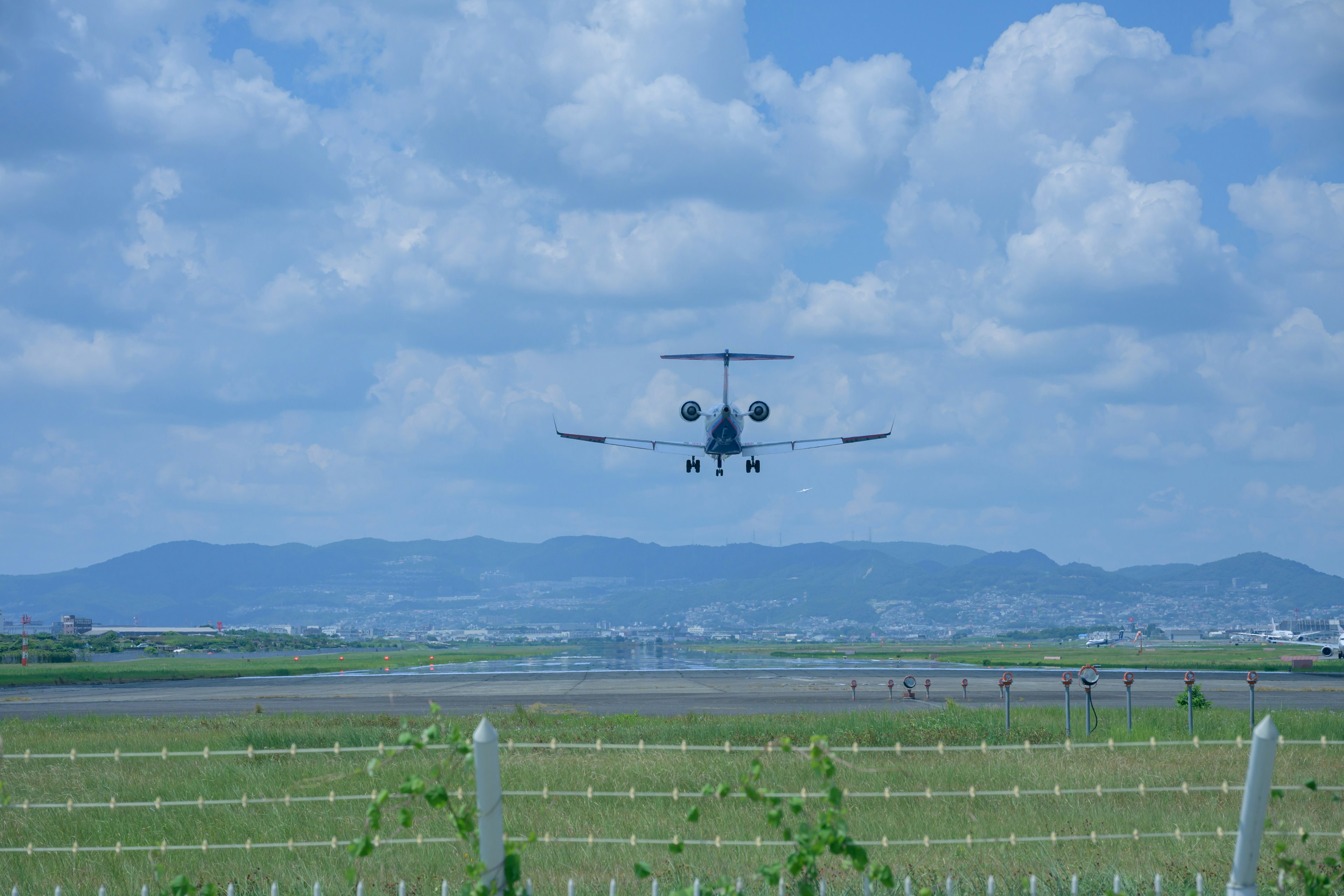 Ein Flugzeug landet unter einem blauen Himmel mit Wolken und grünem Gras