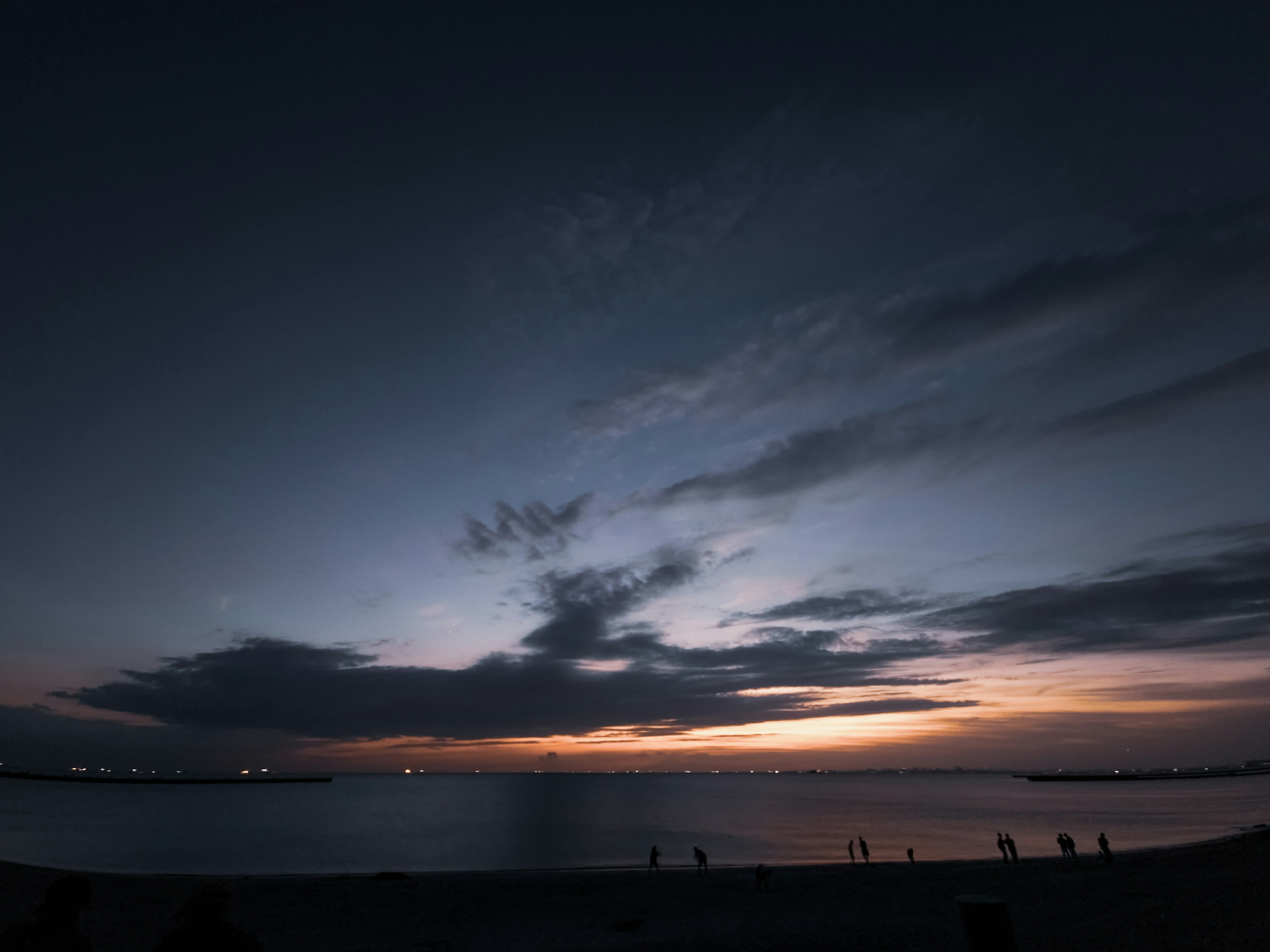 A coastal sunset with dark sky and clouds over the water