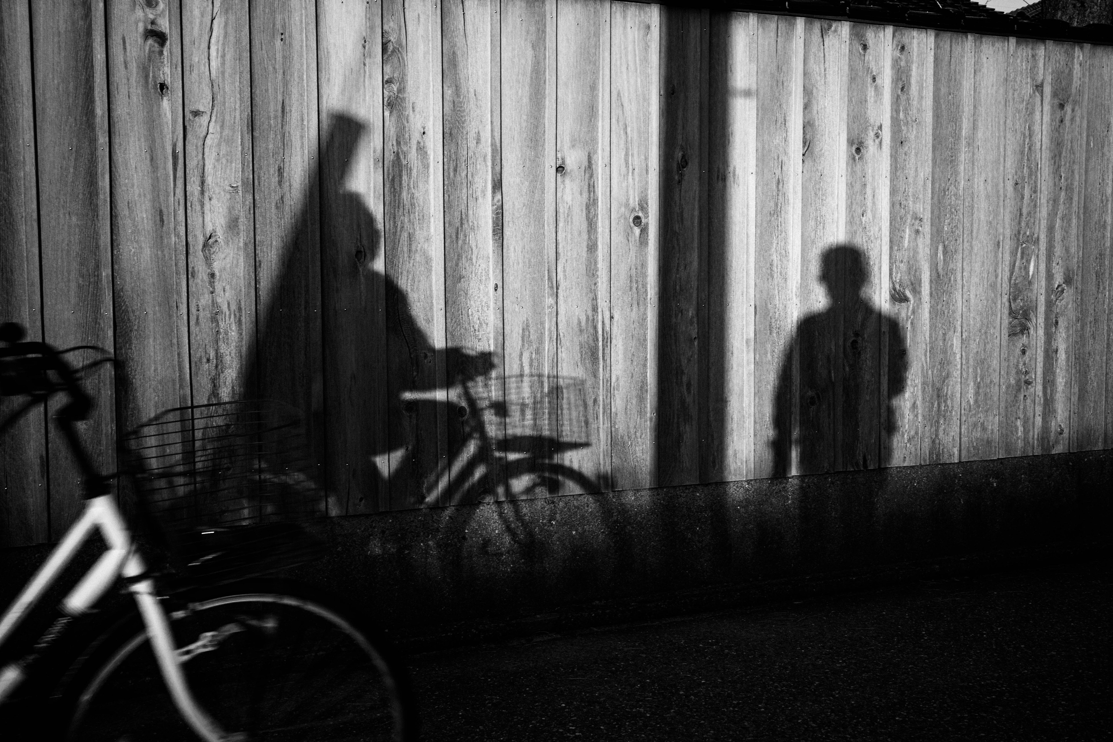 Sombras de una persona en bicicleta y un niño contra una cerca de madera