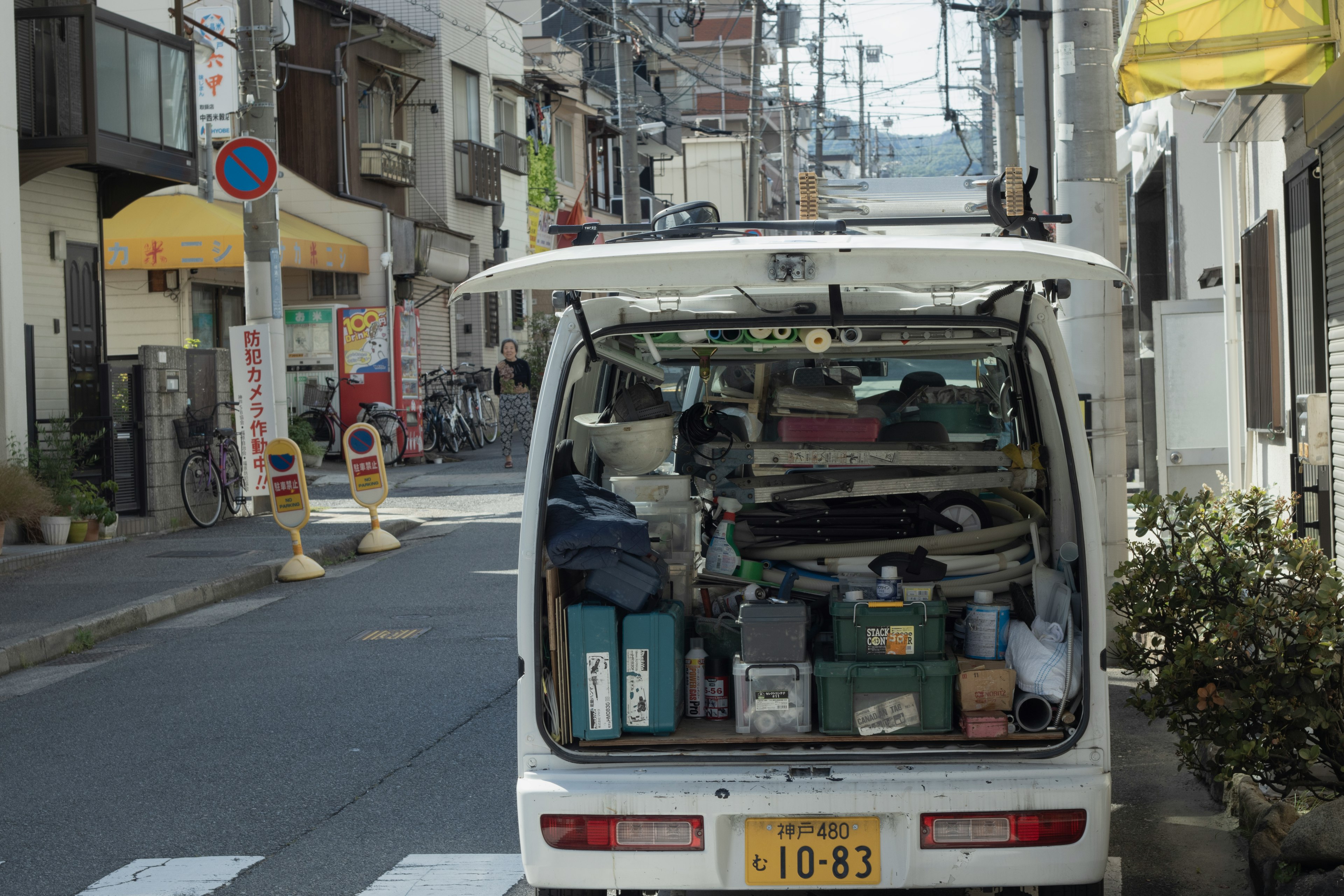 狭い通りに停車した白いバンの後部に、さまざまな道具や用品が詰まっている