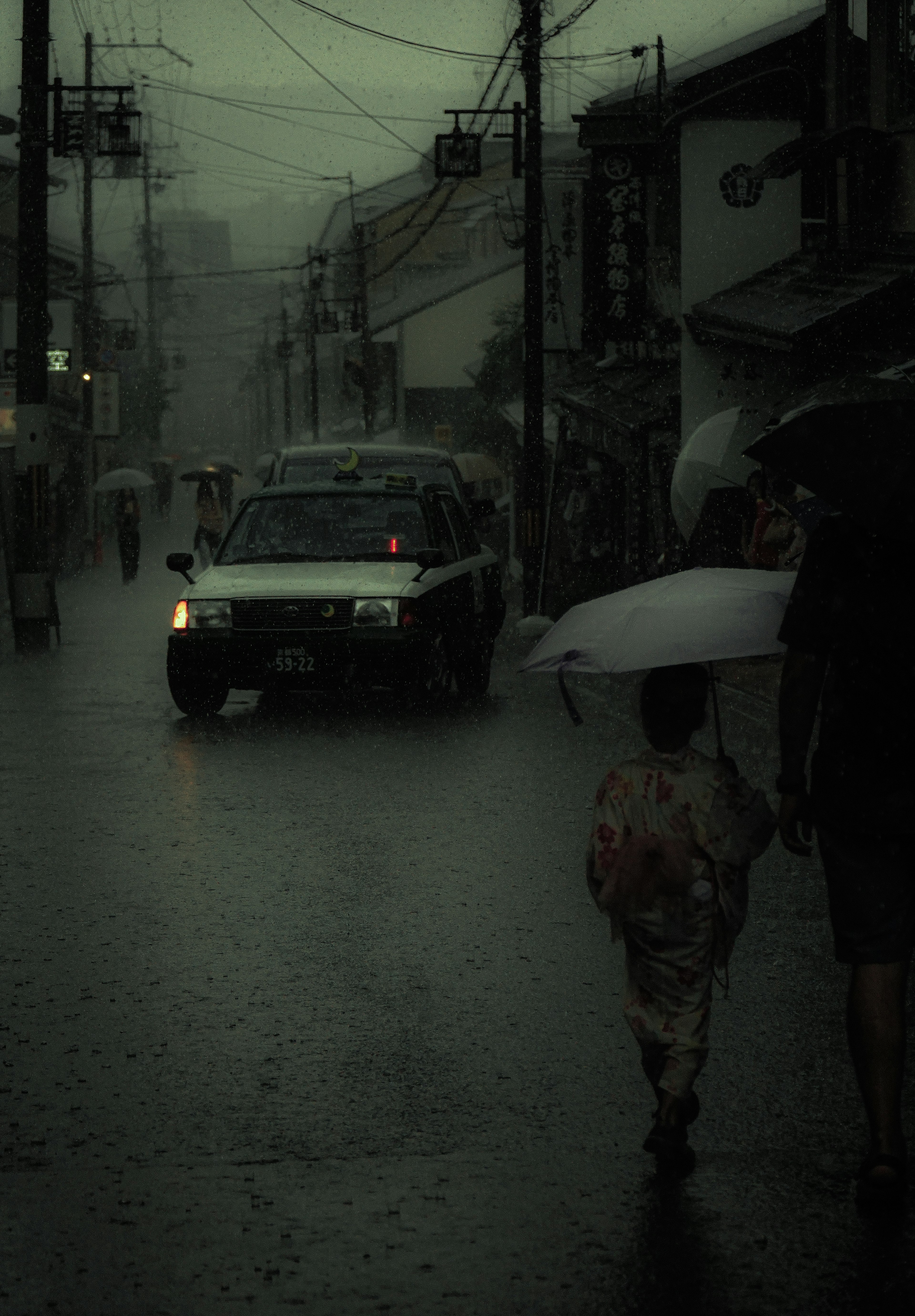 暗い雨の日の街並みに傘を持つ子供と大人が歩いている