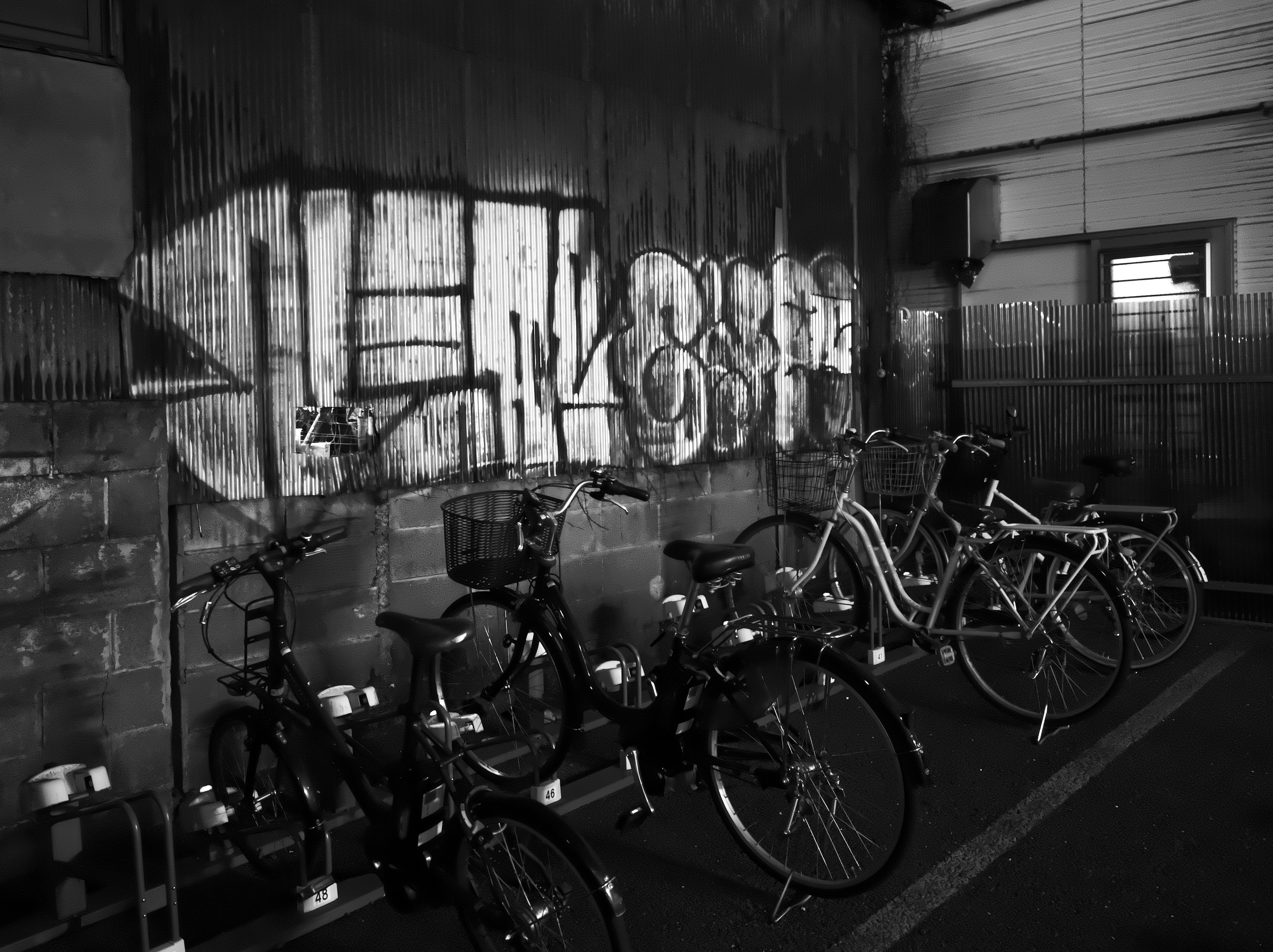 Scène en noir et blanc avec des vélos et des graffitis sur le mur