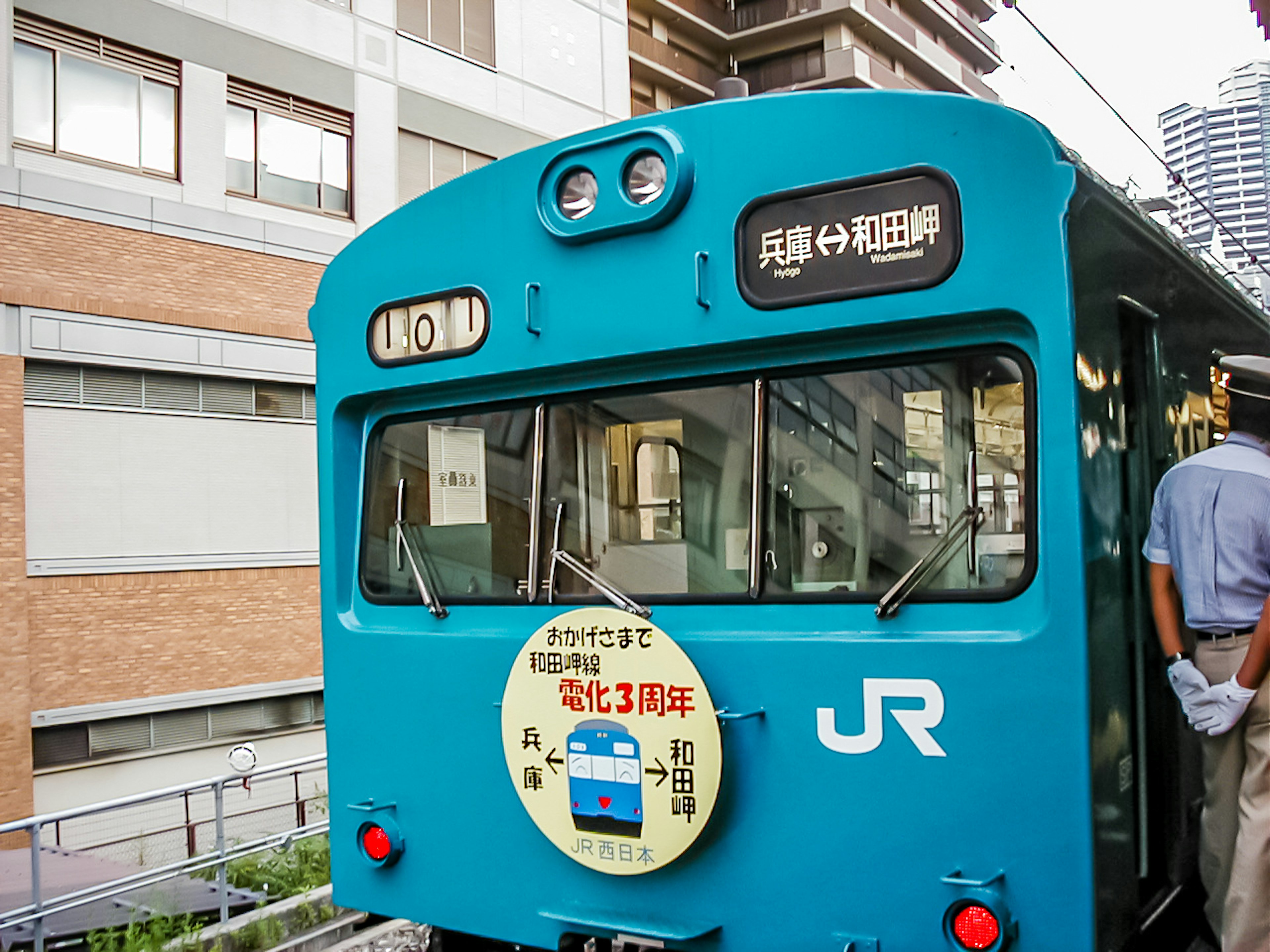 Vista posteriore di un treno JR blu con un conducente in piedi