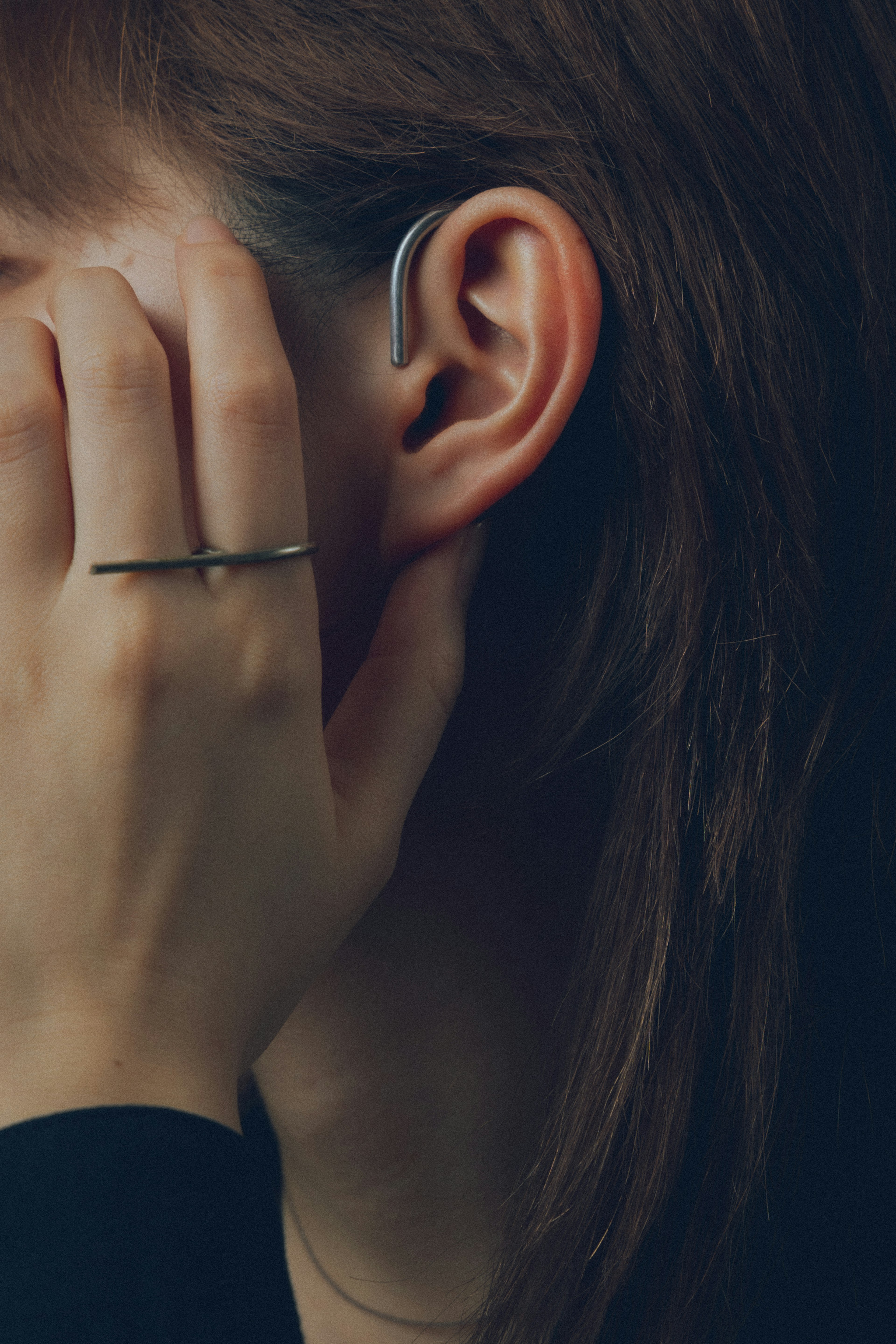 Profil d'une femme partiellement cachée par sa main portant un appareil auditif à l'oreille et une simple bague au doigt