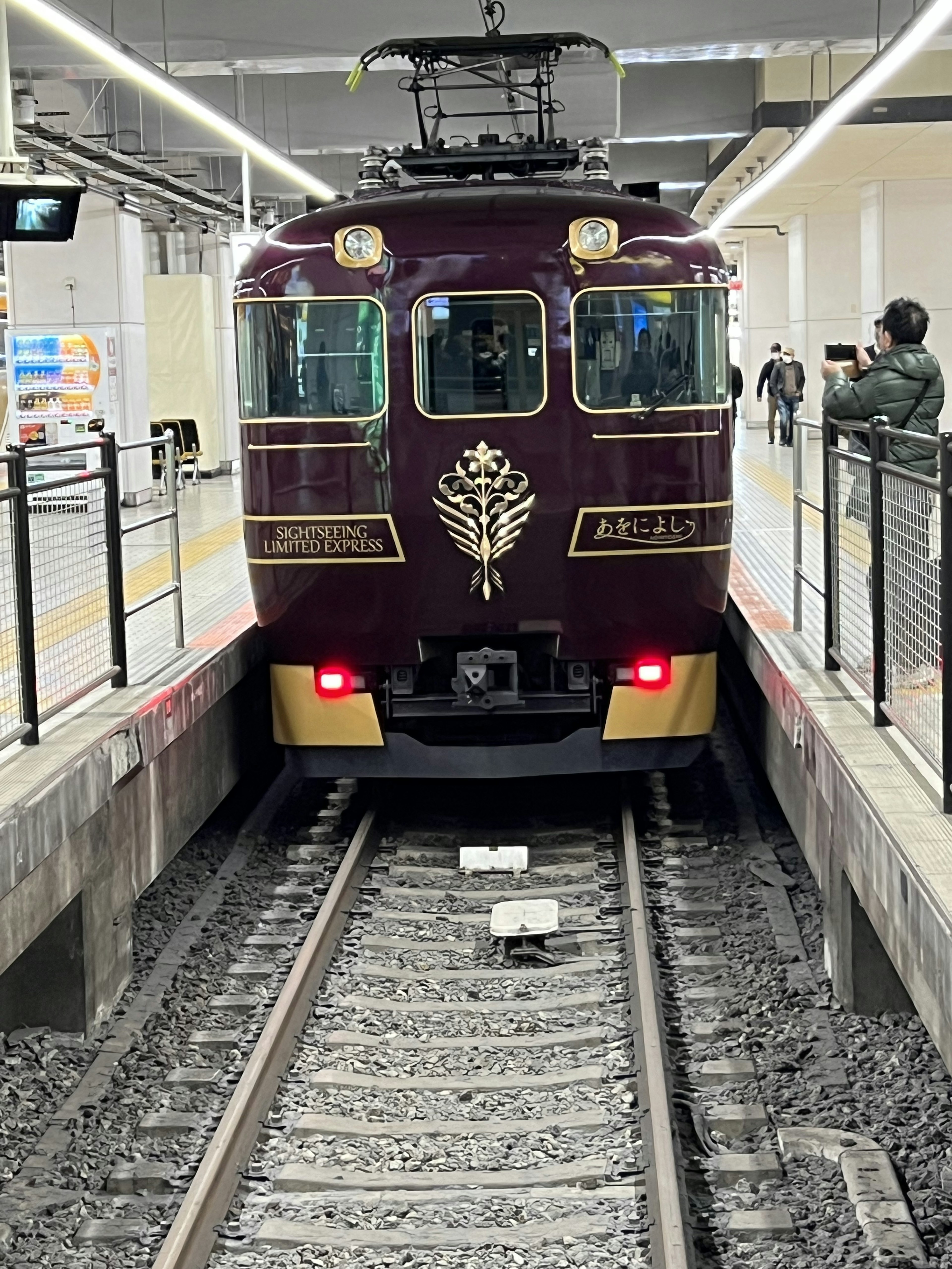 Un train violet arrivant à une station avec des passagers attendant