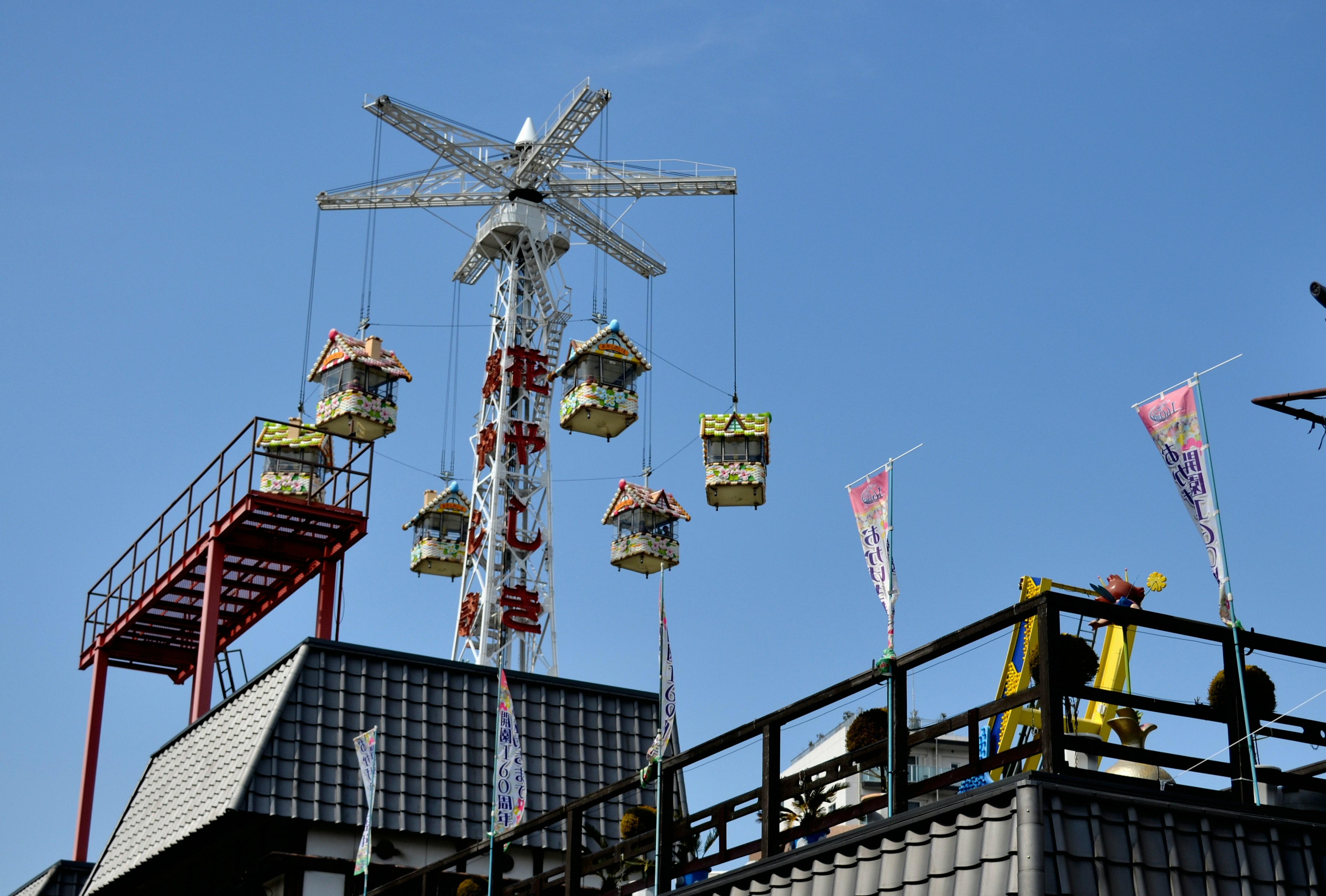 Hängende Attraktion, die einem Riesenrad ähnelt, unter einem blauen Himmel mit umliegenden Gebäuden