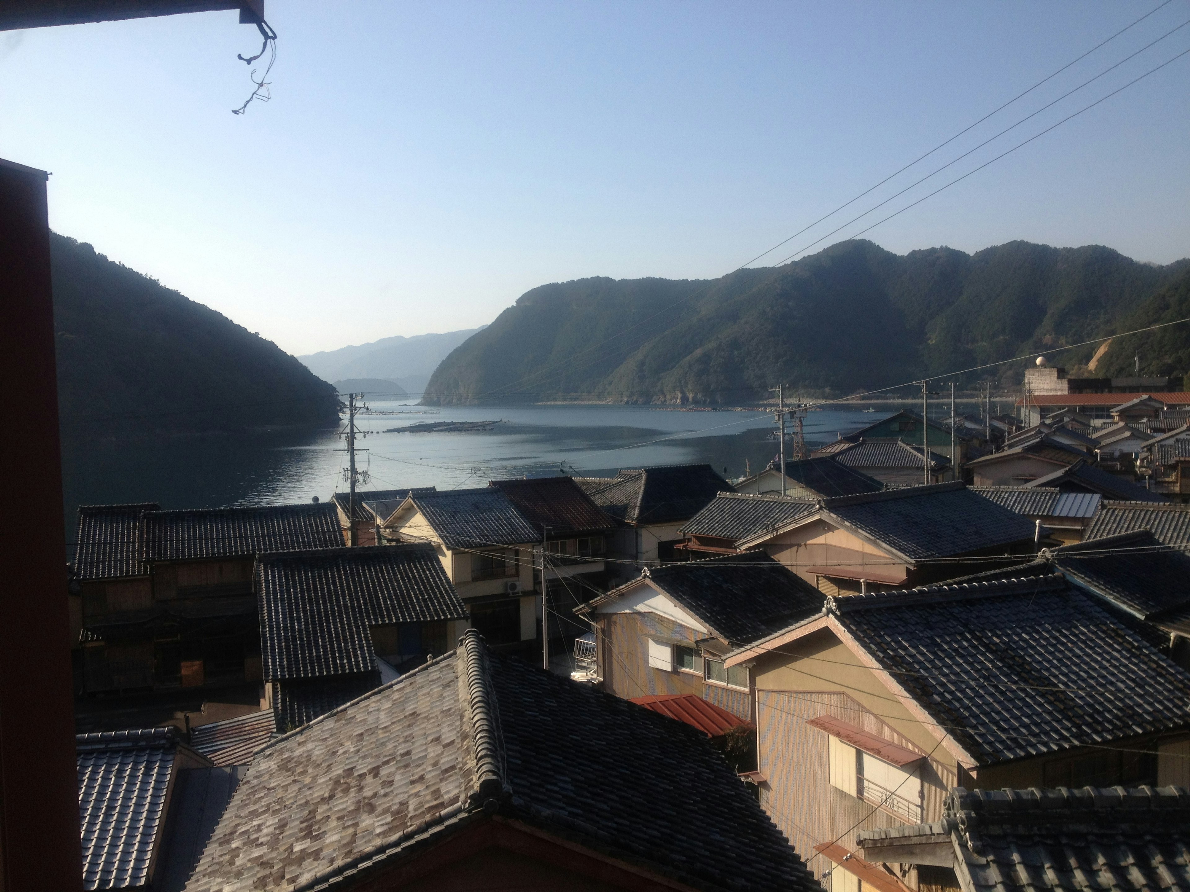 Vue d'un village japonais traditionnel avec une mer calme et des montagnes en arrière-plan