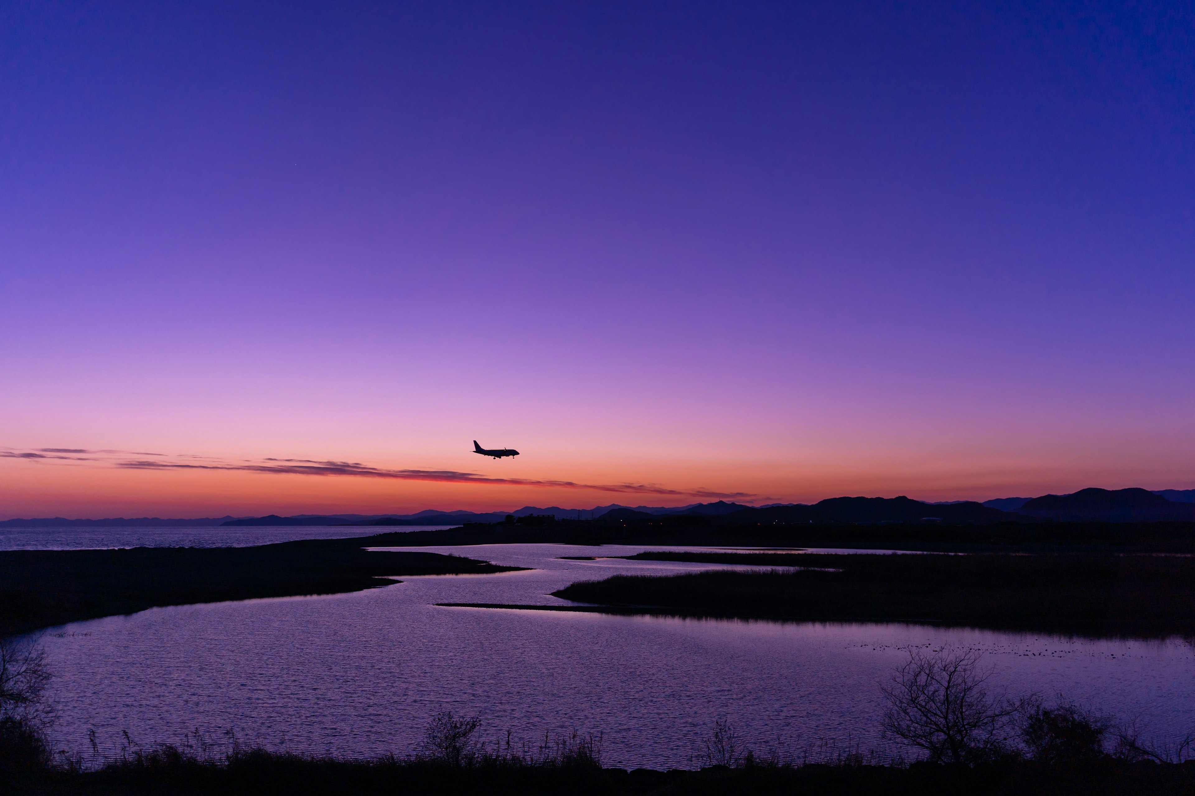 夕暮れ時の空を飛ぶ飛行機と河川の美しい風景