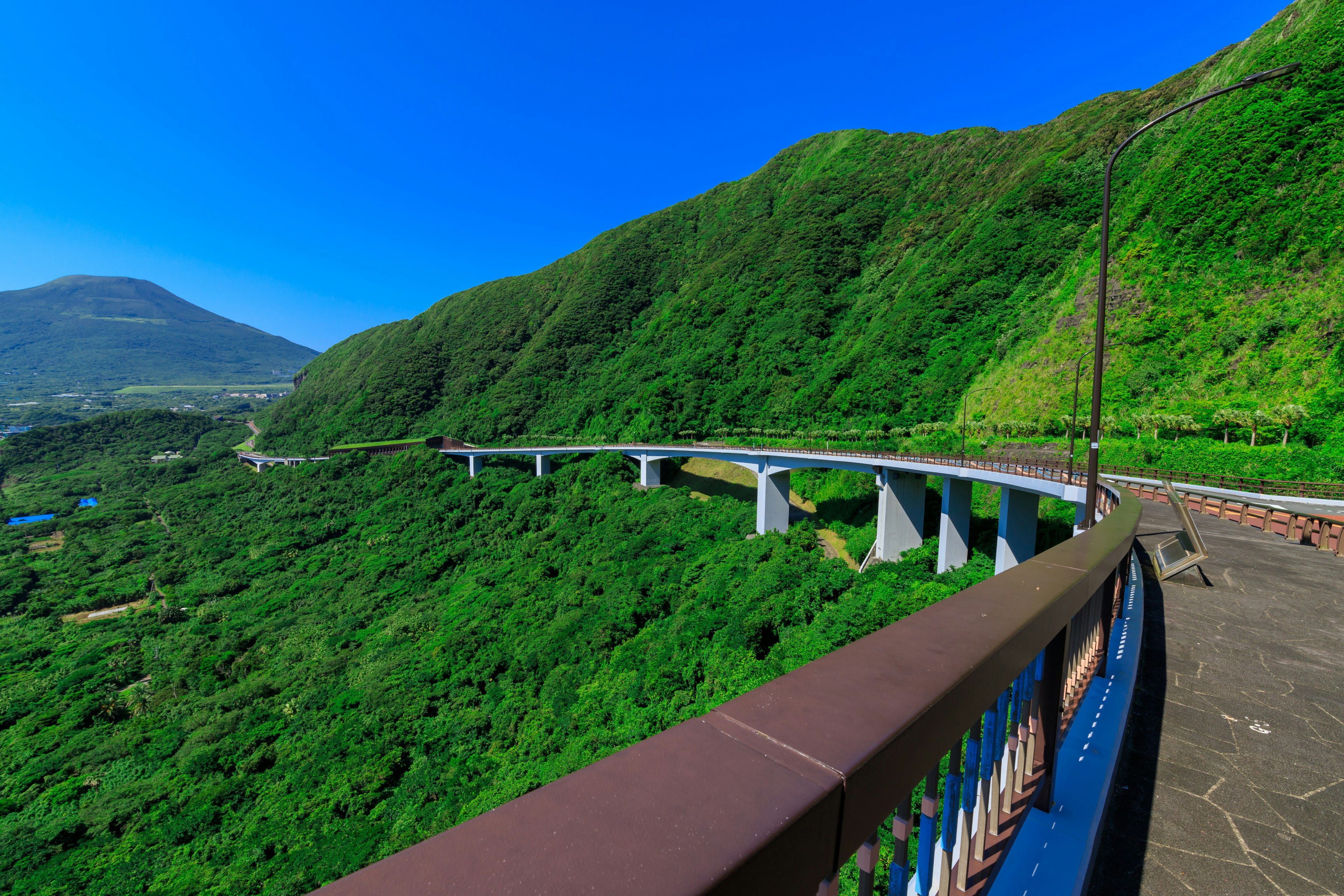 Pemandangan jembatan yang dikelilingi oleh pegunungan hijau subur dan langit biru yang cerah