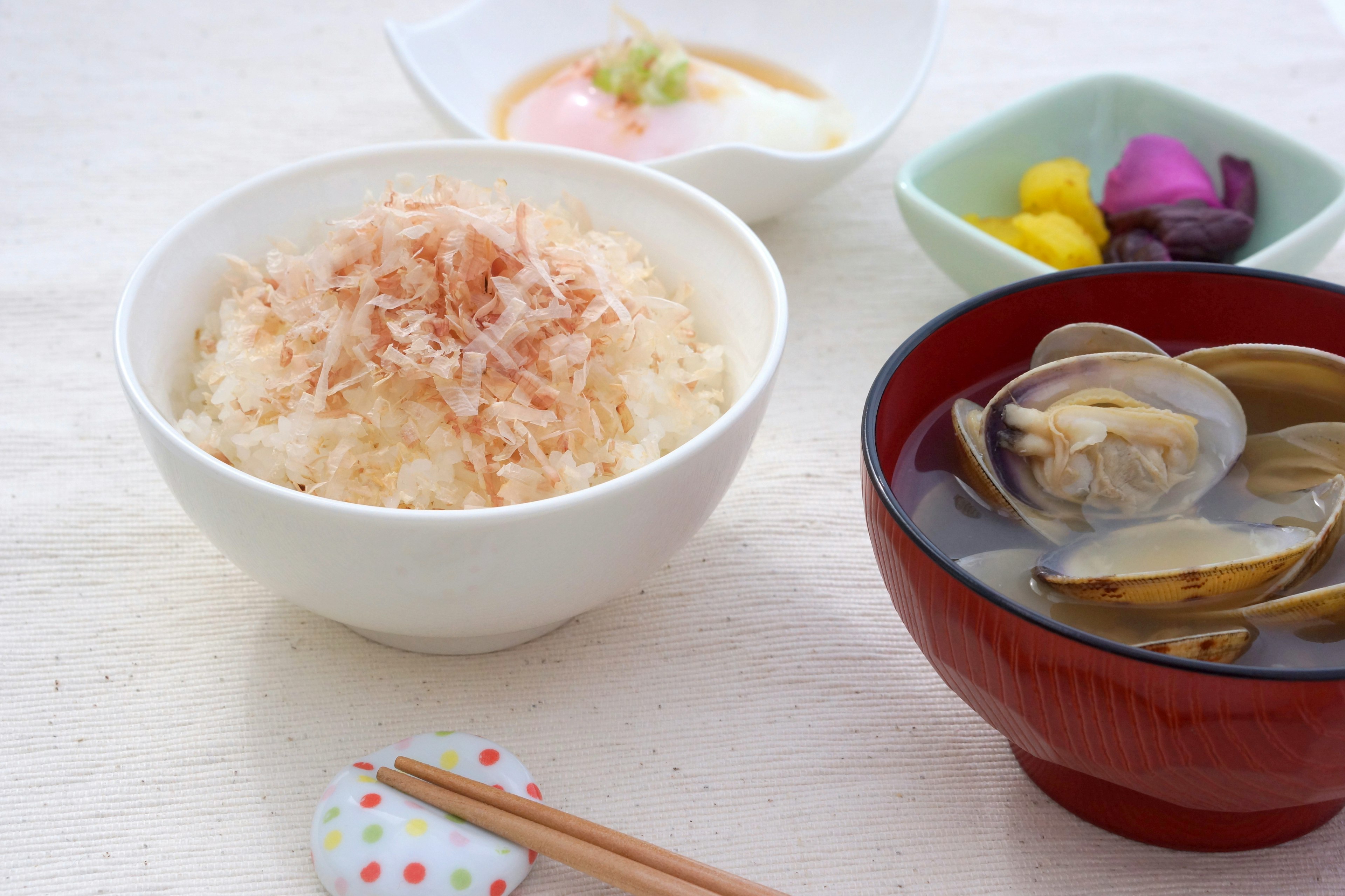 Bol de riz blanc garni de flocons de bonite avec un bol rouge de soupe miso aux palourdes