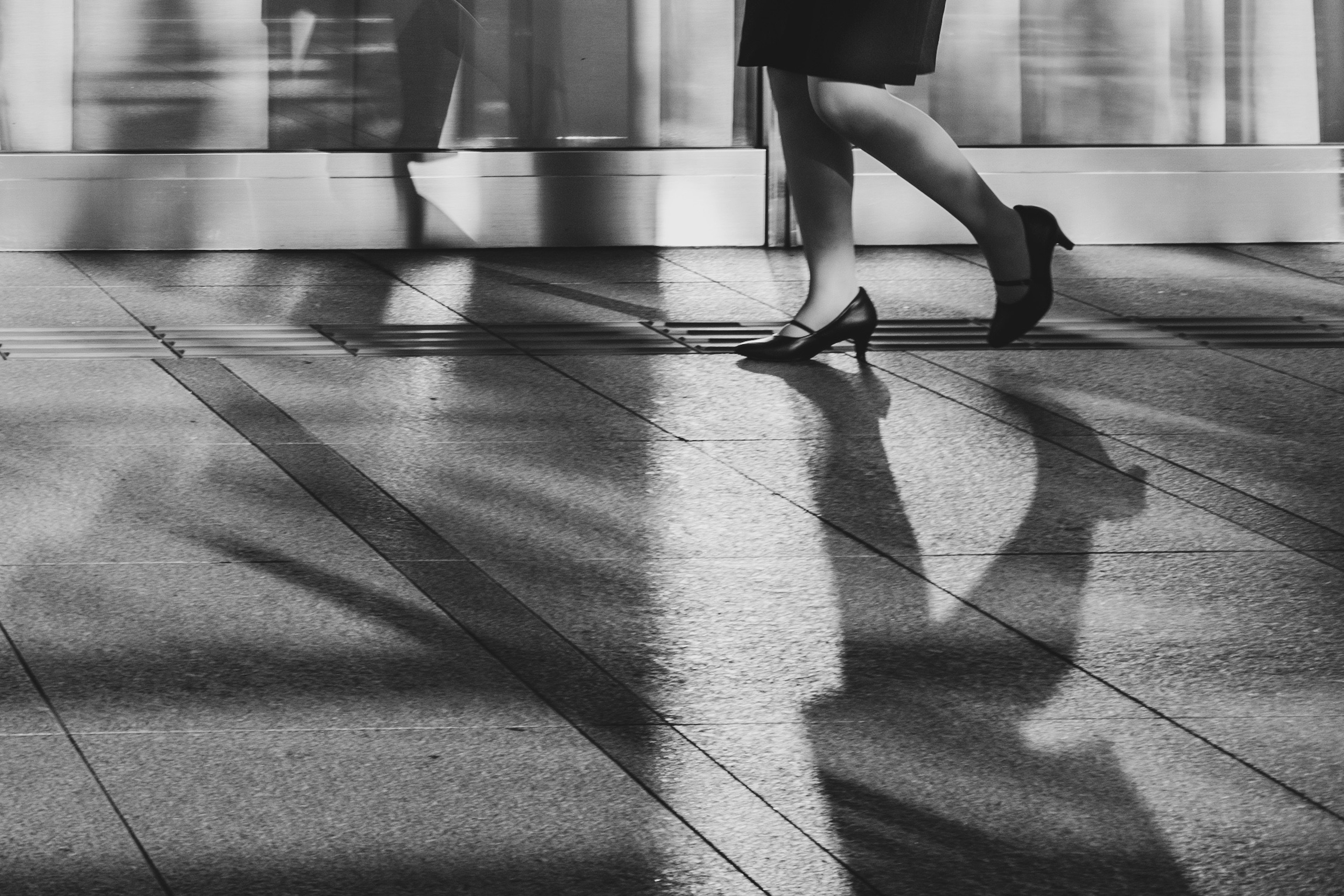 Immagine in bianco e nero delle gambe di una donna che cammina con lunghe ombre sul pavimento