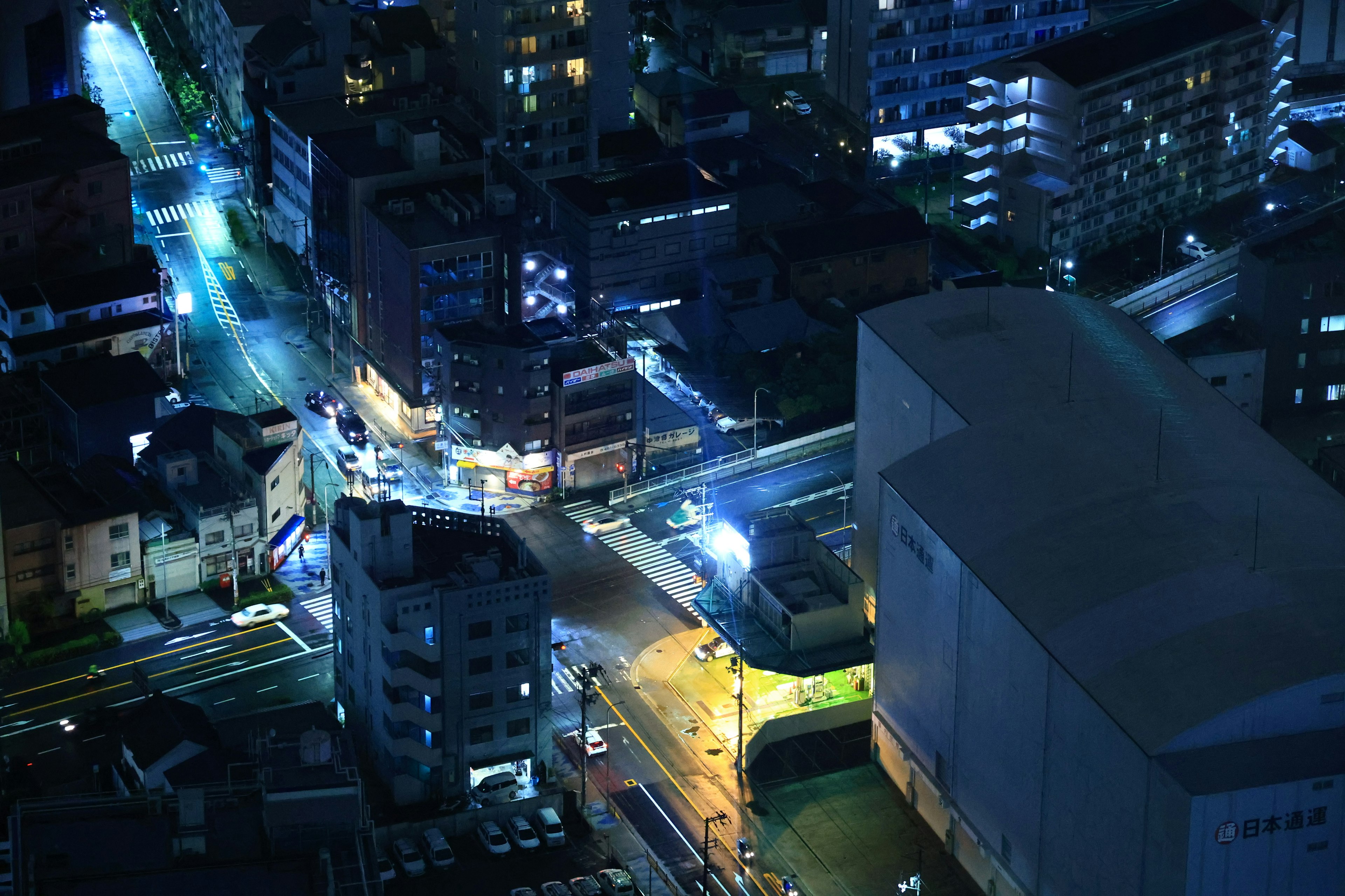 Night cityscape featuring high-rise buildings and road intersections illuminated by blue lights