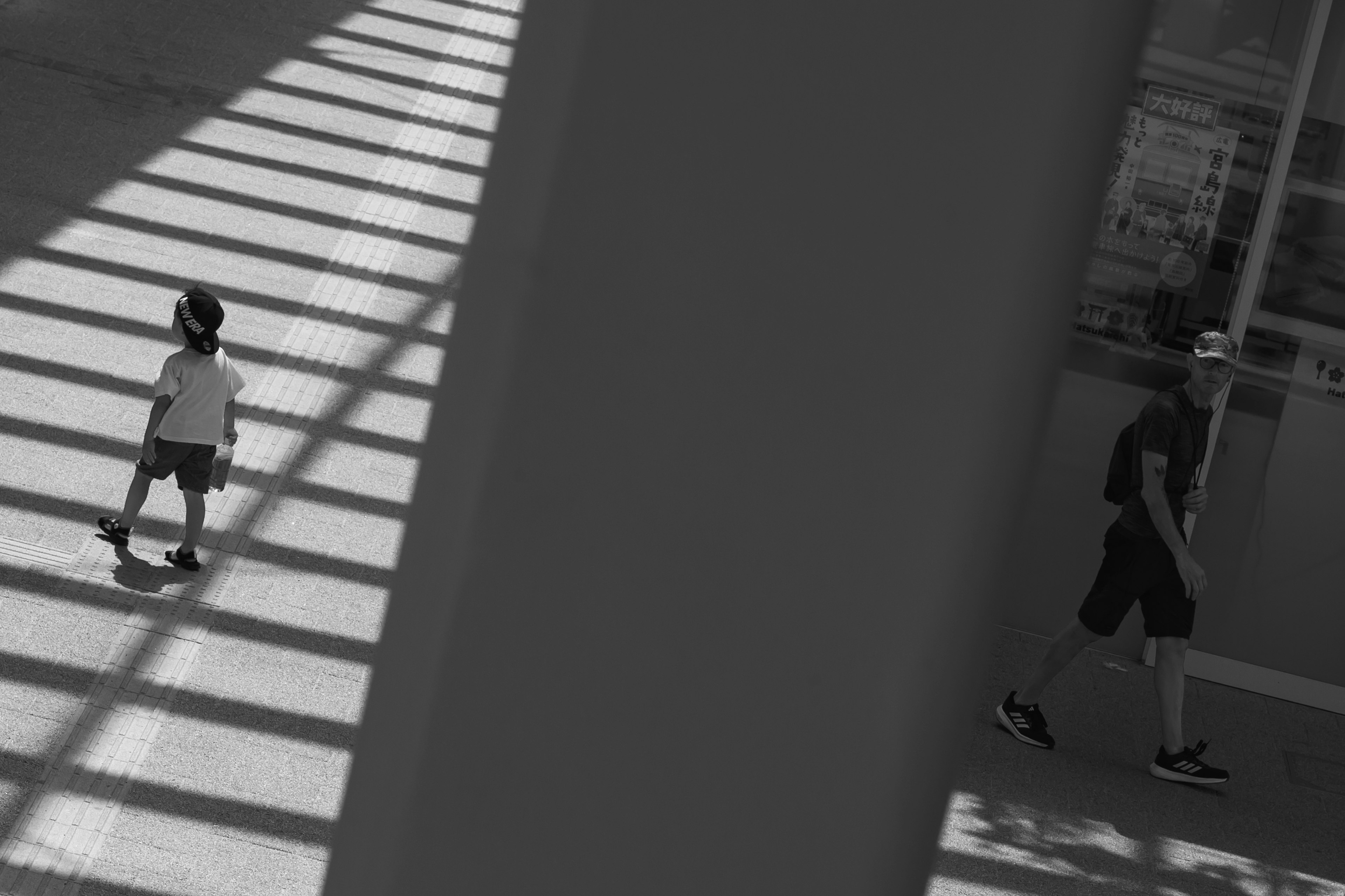 Foto en blanco y negro de un niño y un adulto caminando a través de sombras a rayas en el suelo