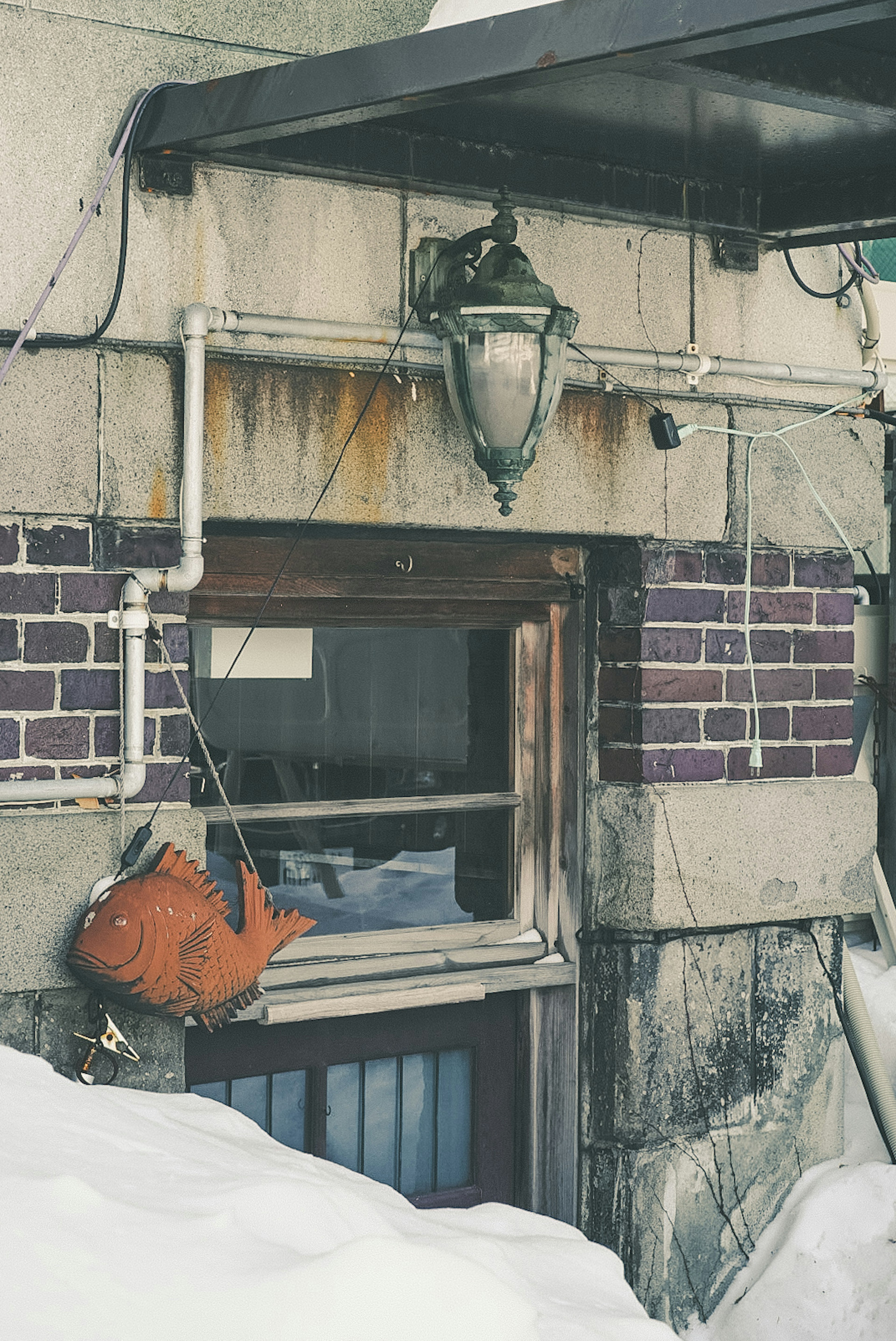 Old building window covered in snow with an orange bag hanging