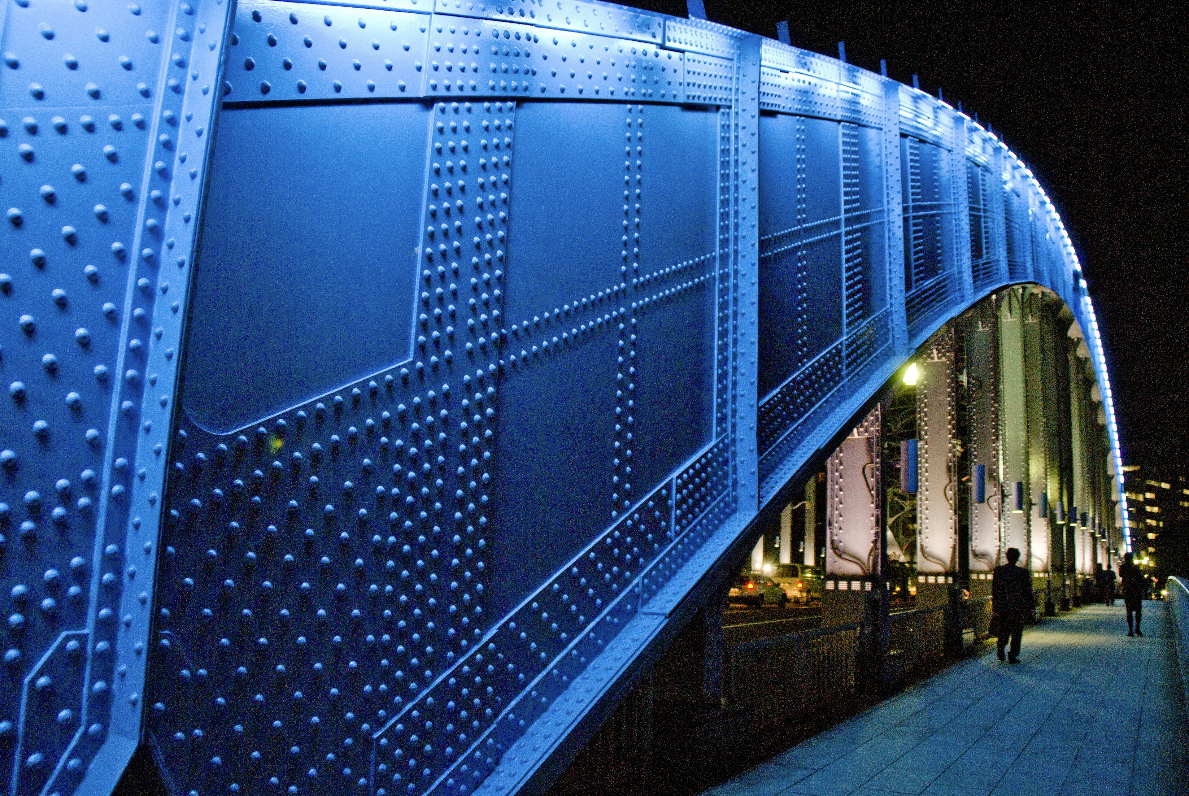 Side view of a blue bridge at night with rivets