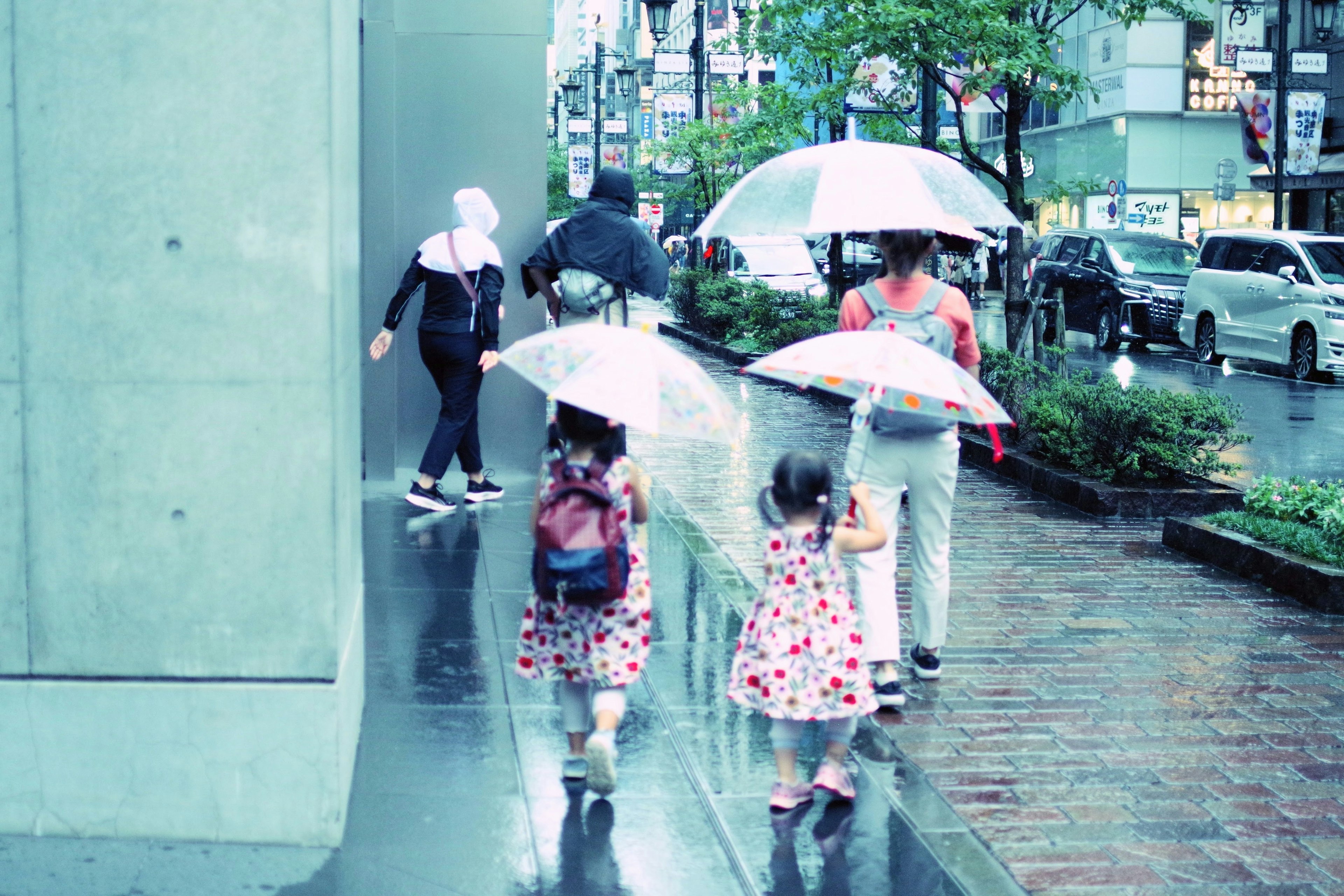 雨の中で傘を持って歩く子供たちと大人たちのグループ