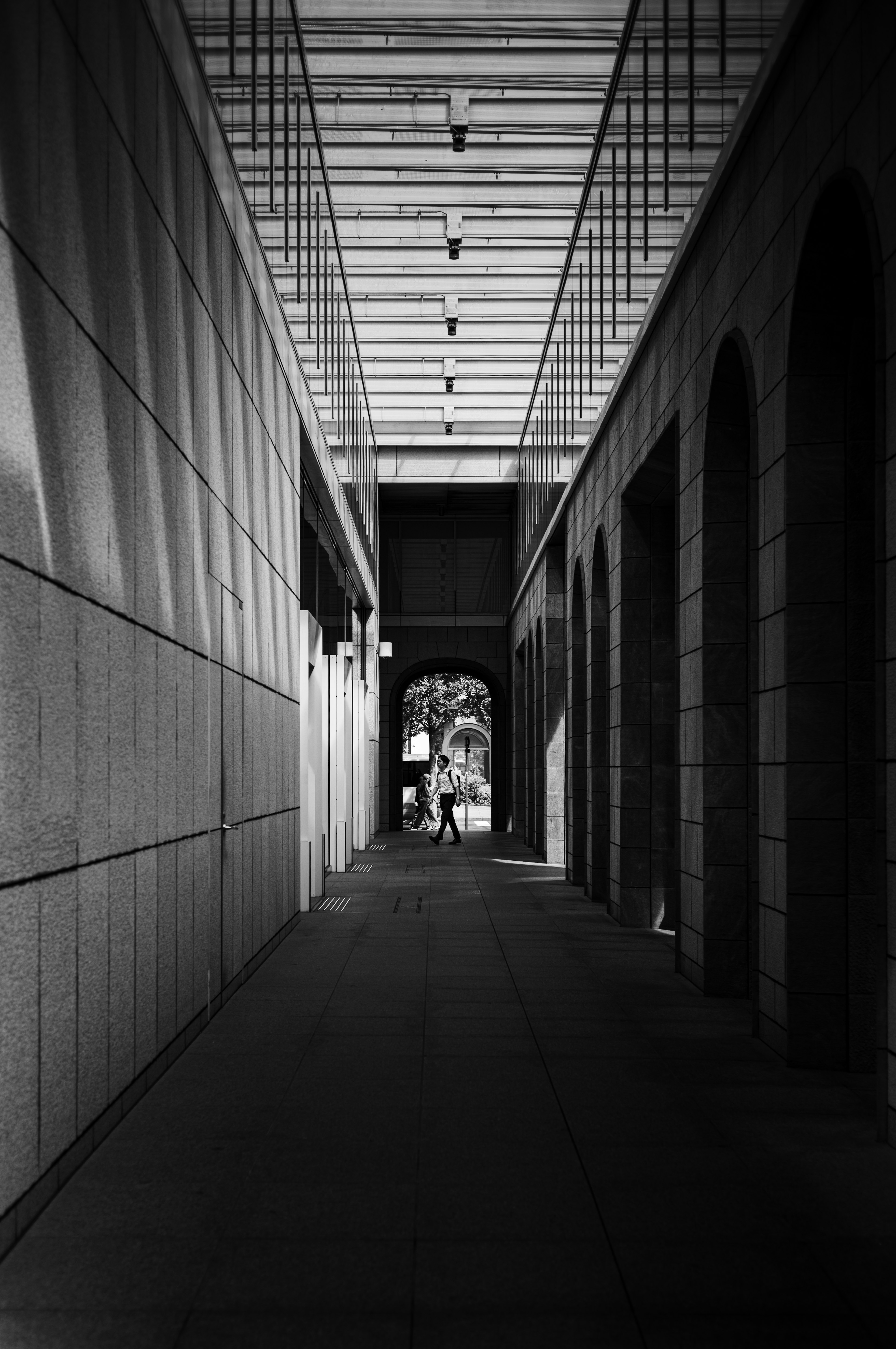 Couloir en noir et blanc avec des arches menant au loin Lumière tombant du plafond