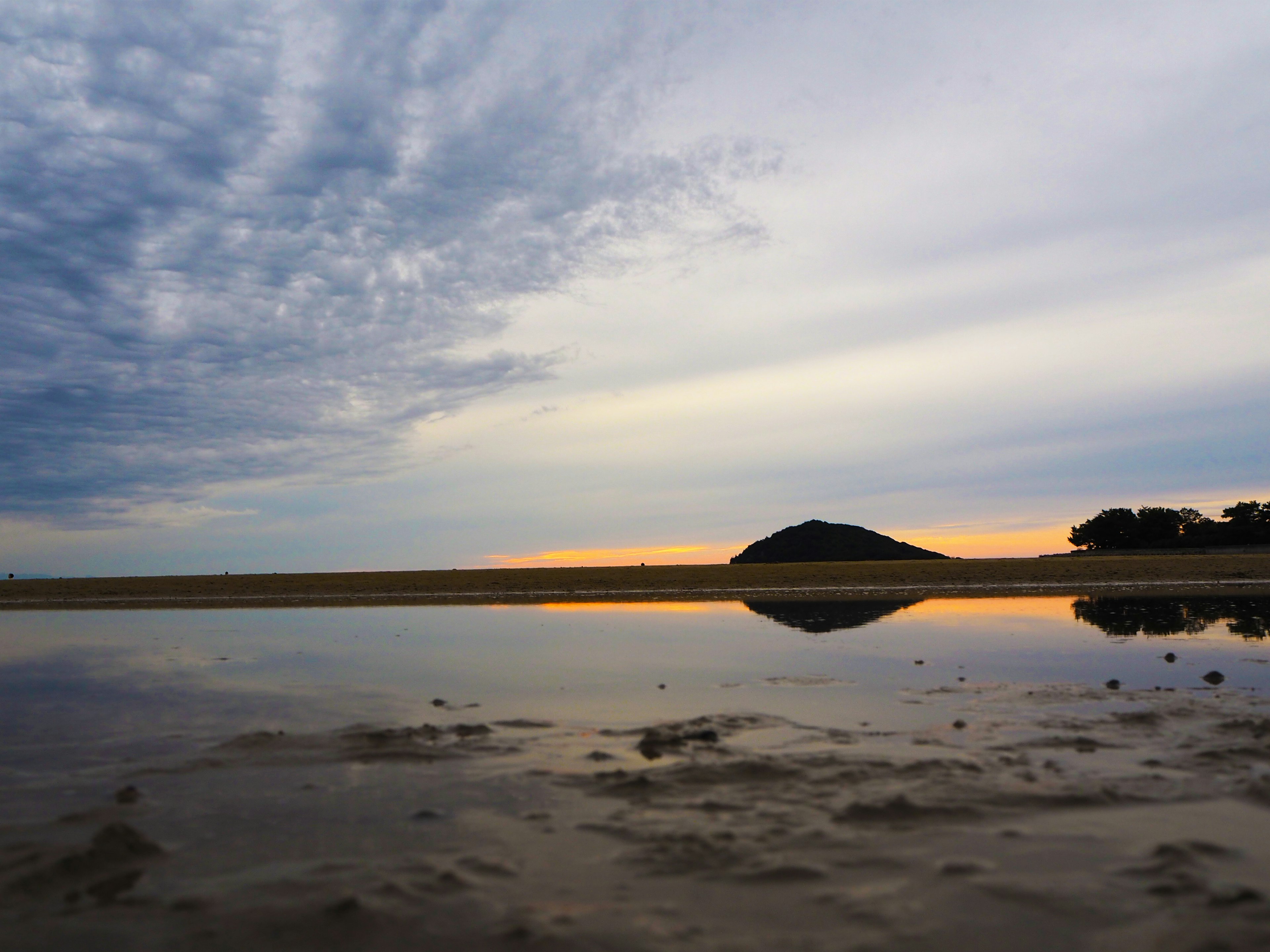 Ruhige Strandszene mit Wolkenreflexionen beim Sonnenuntergang