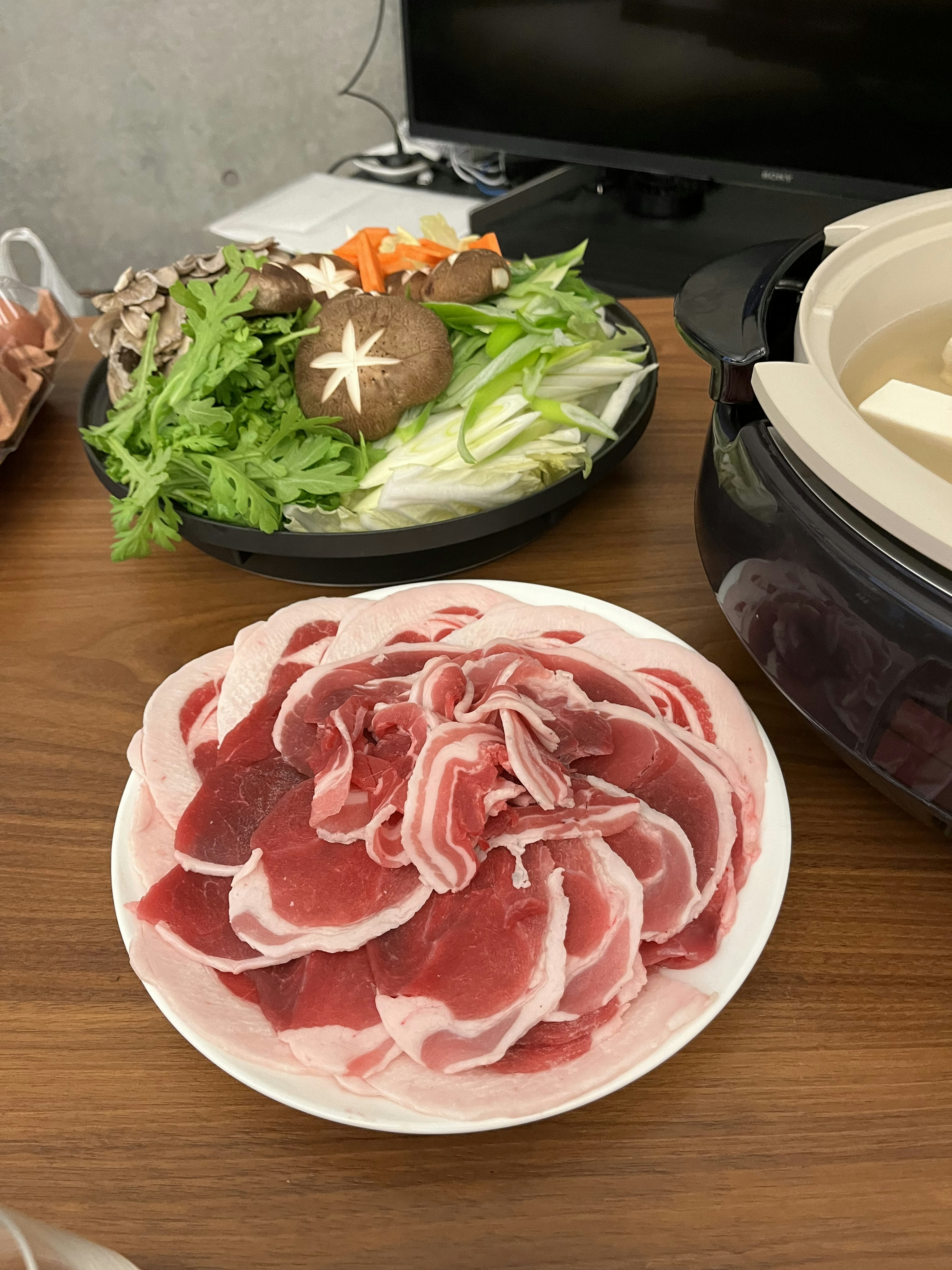 Carne en rodajas dispuesta en forma de rosa en un plato con verduras frescas al fondo