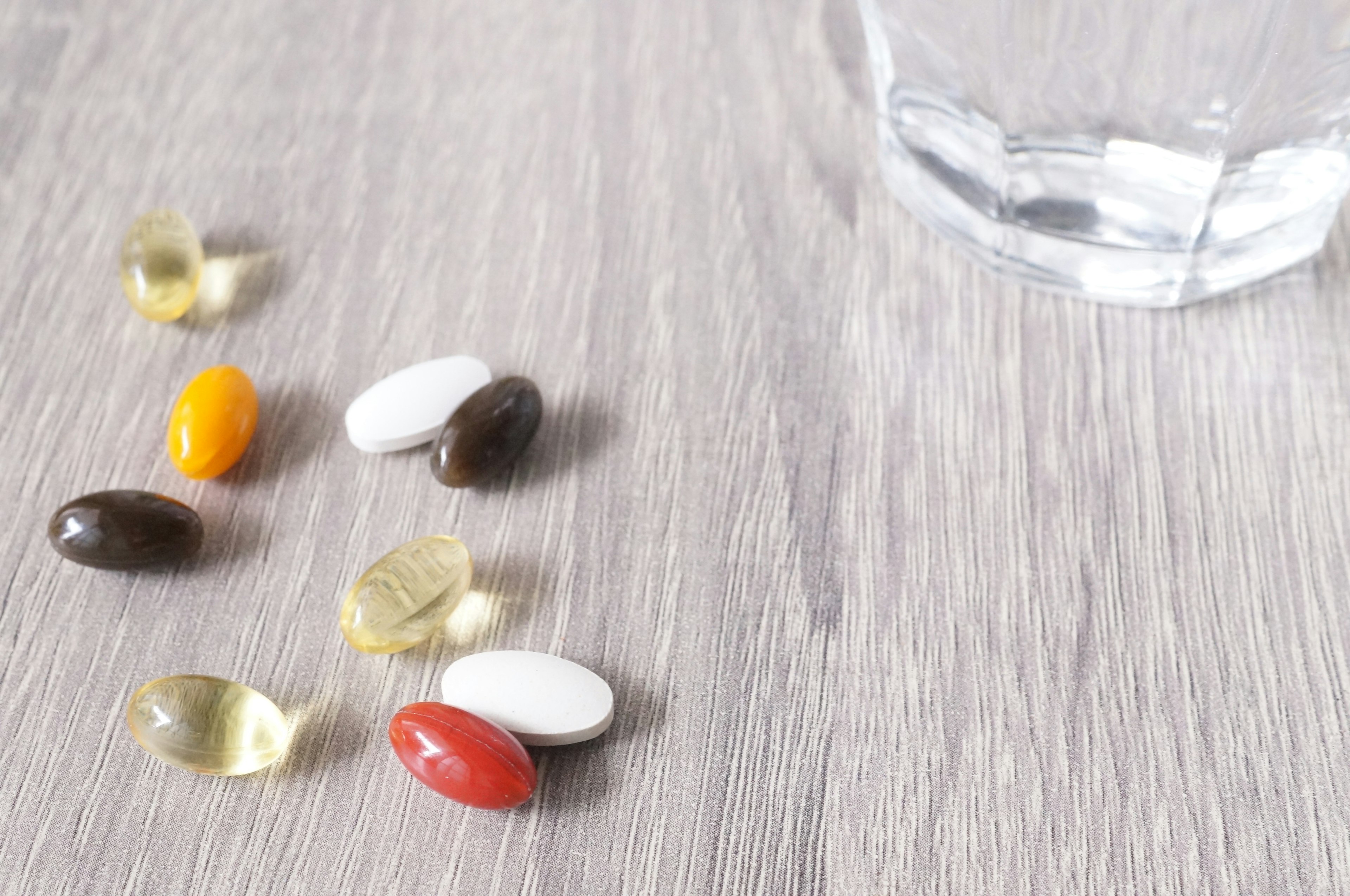 Various colored supplements and capsules near a glass of water