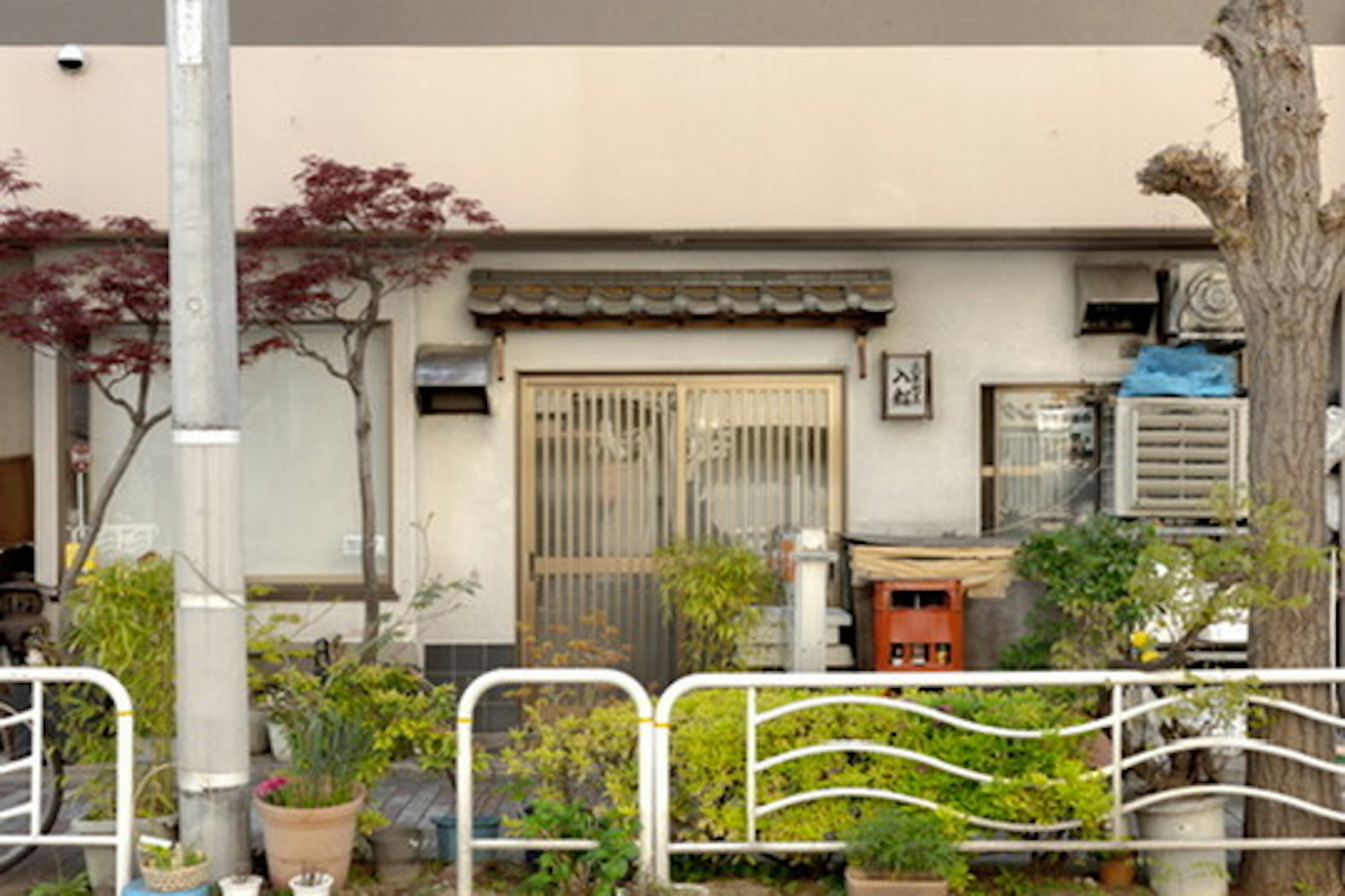 Exterior de una pequeña casa japonesa con plantas y cerca