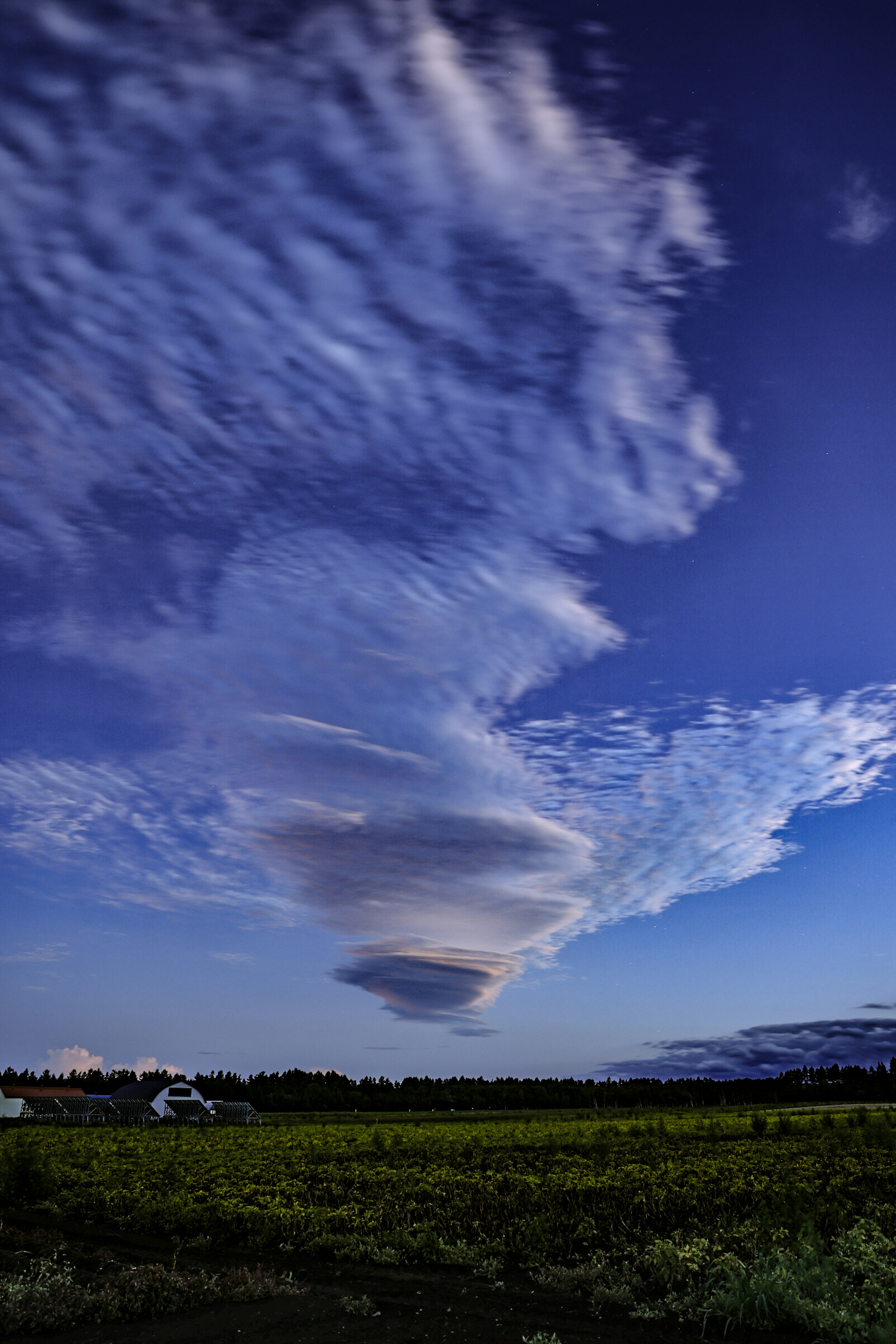 Spiralwolken vor blauem Himmel mit grünem Feld