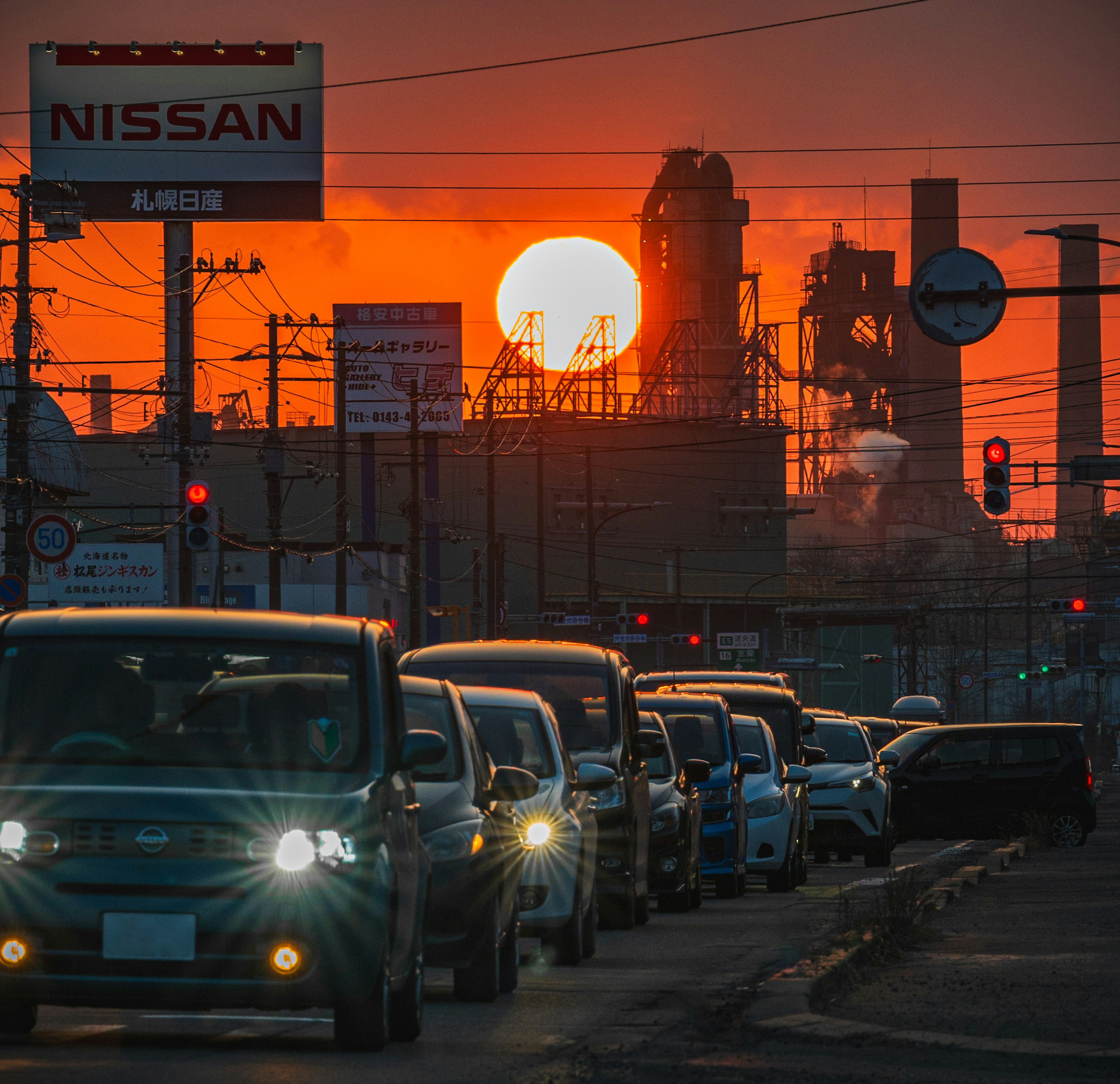 Traffic jam with factories silhouetted against a sunset