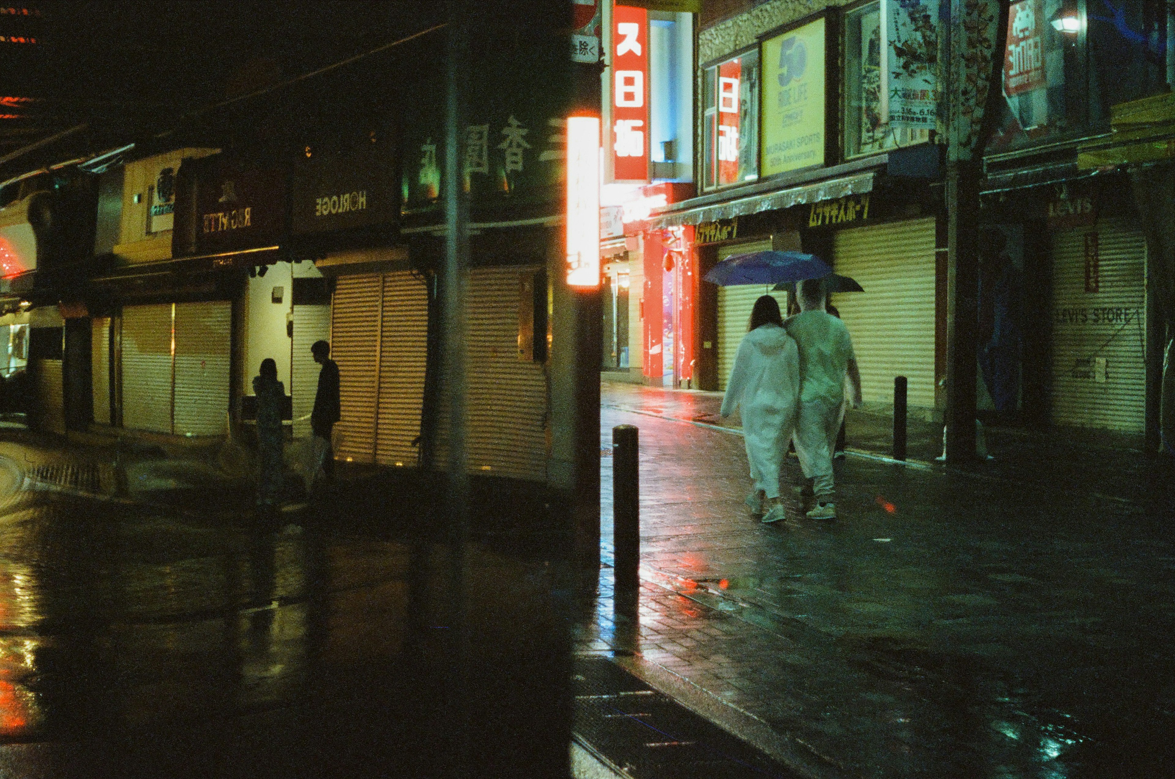 雨の中を歩く人々と閉まった店舗のある夜の街